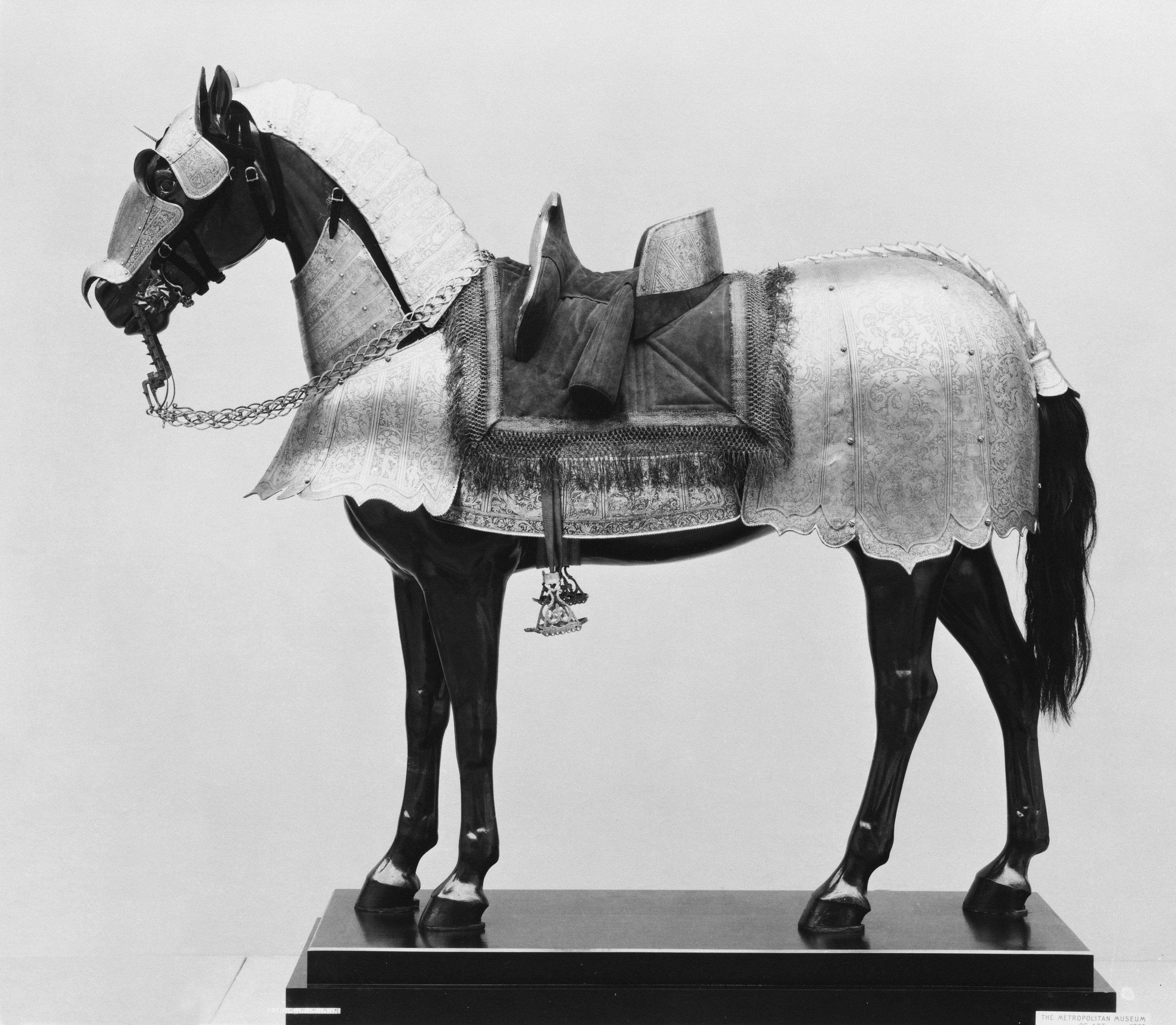 A horse mannequin wearing ornate engraved metal armor and a saddle on a base