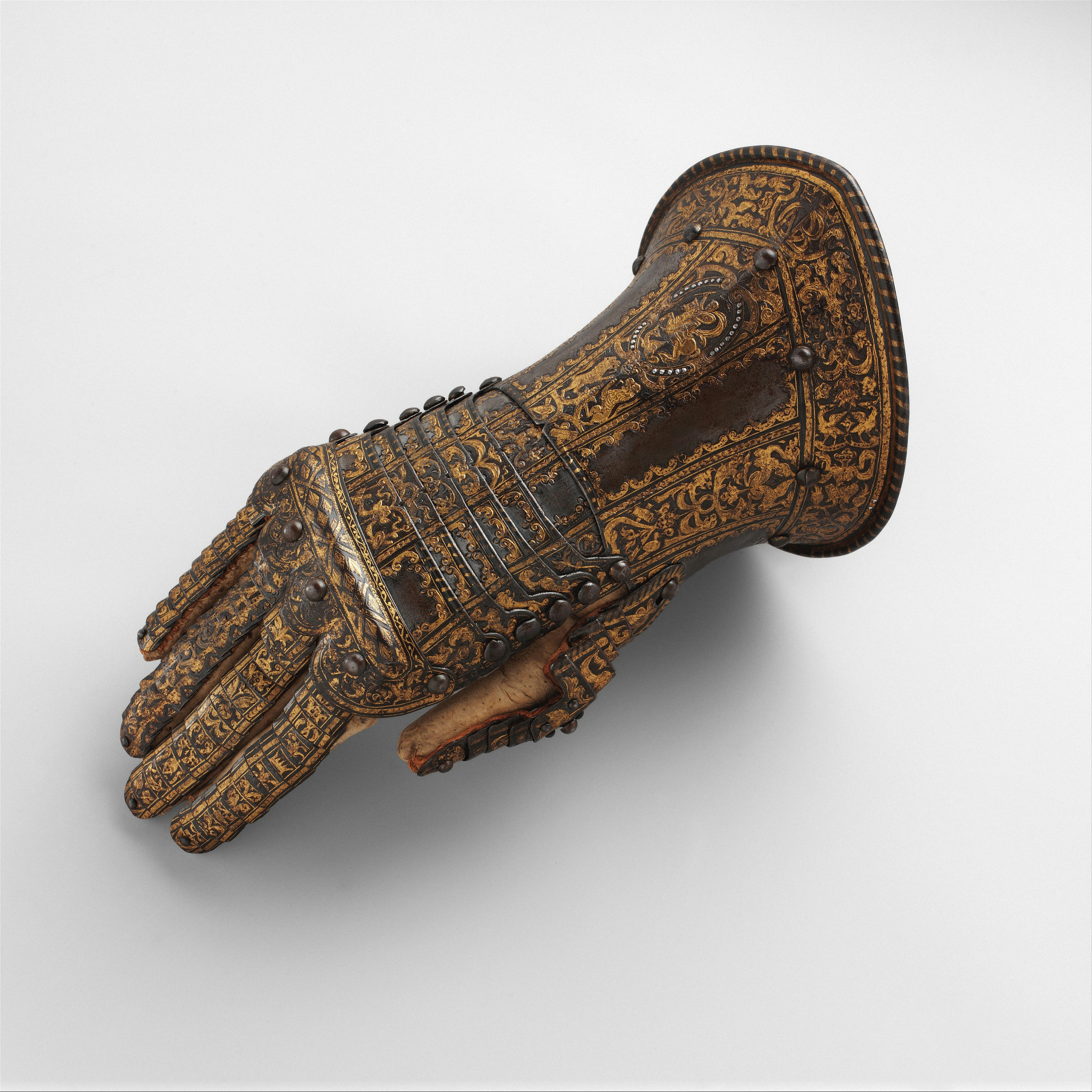 Fotomural An ornate metal gauntlet with intricate gold filigree patterns on a plain background