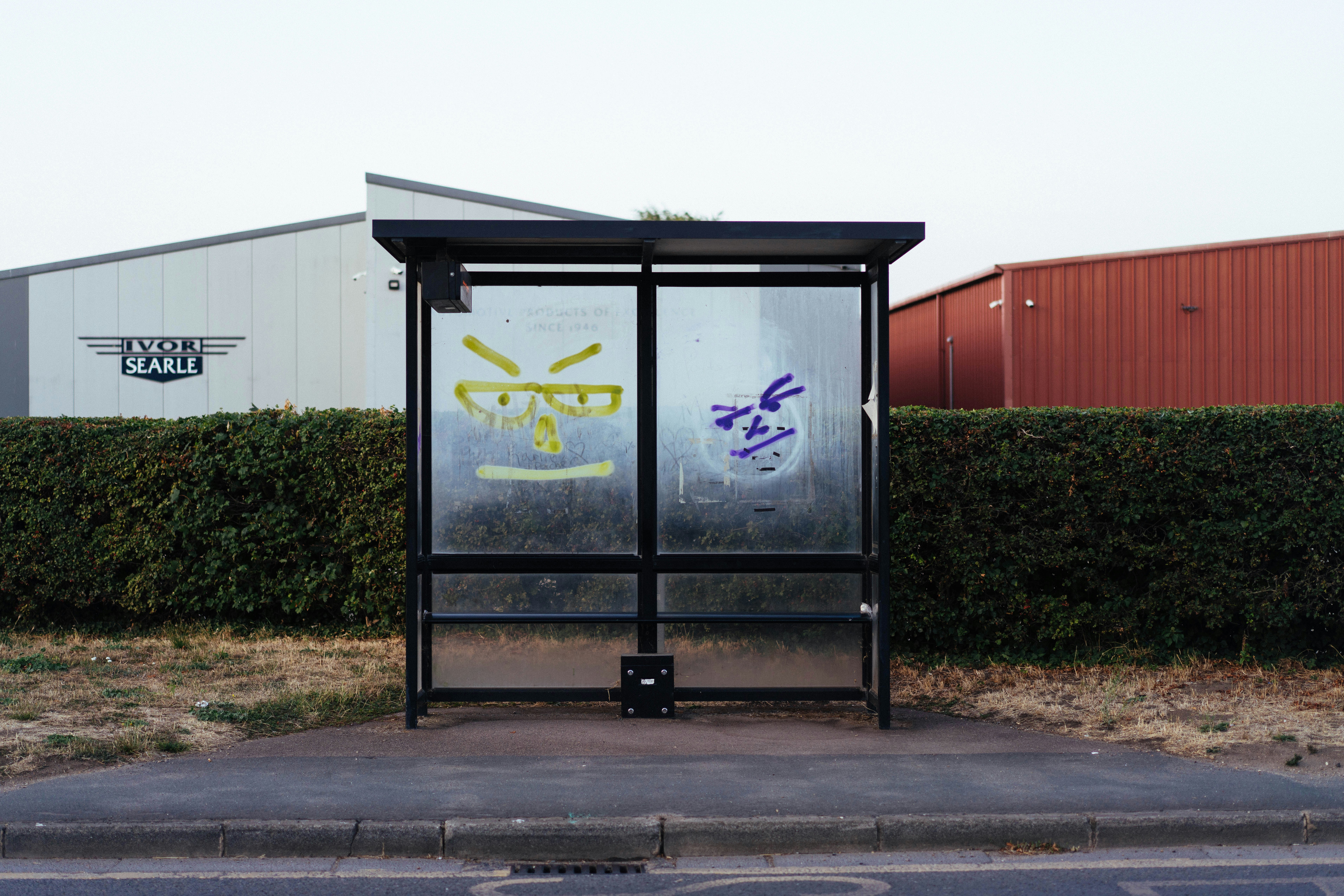 A bus shelter with yellow and purple graffiti faces on the glass panels - 相关推荐