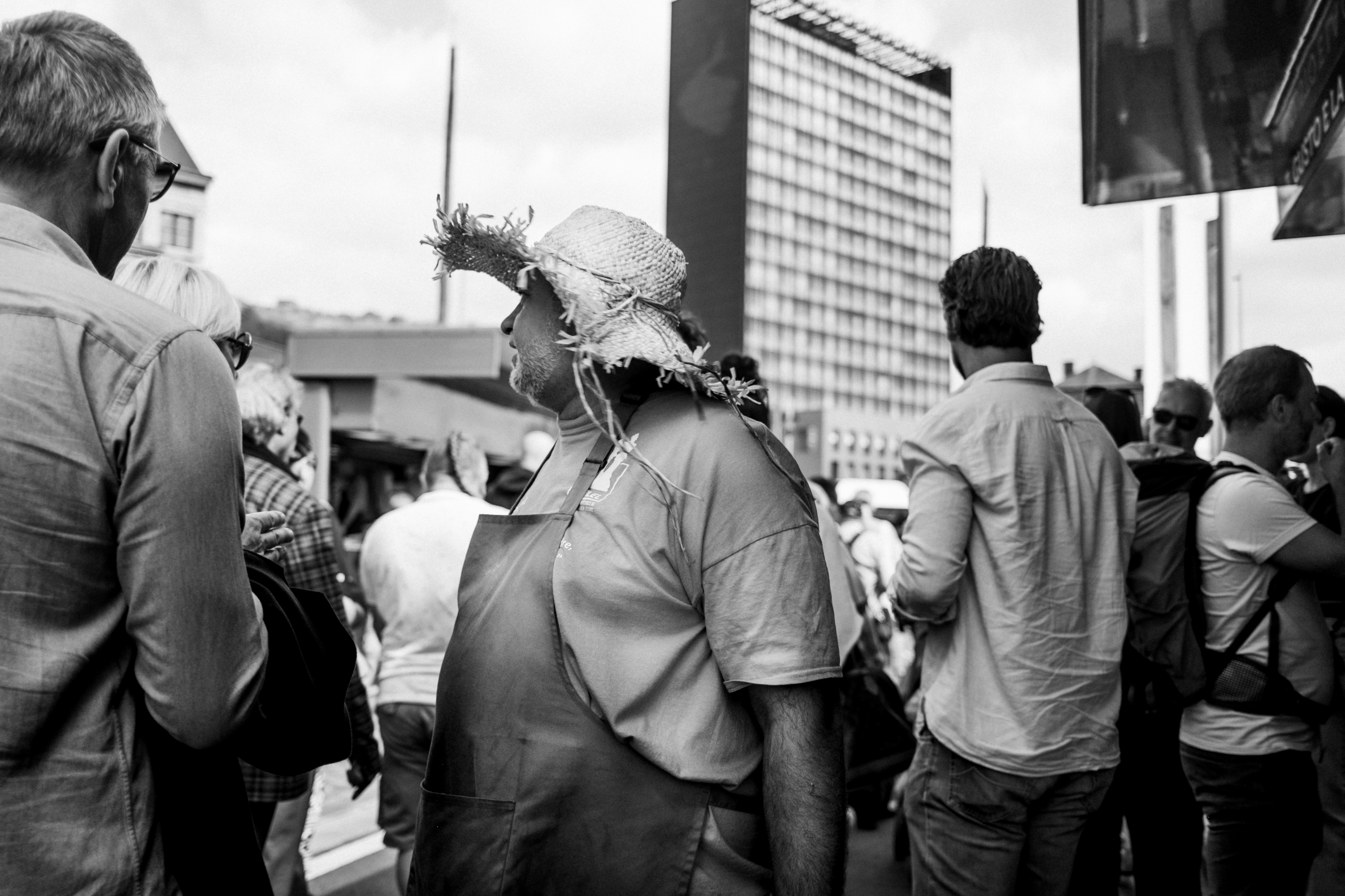 A person in a straw hat and apron among a crowd on a city street