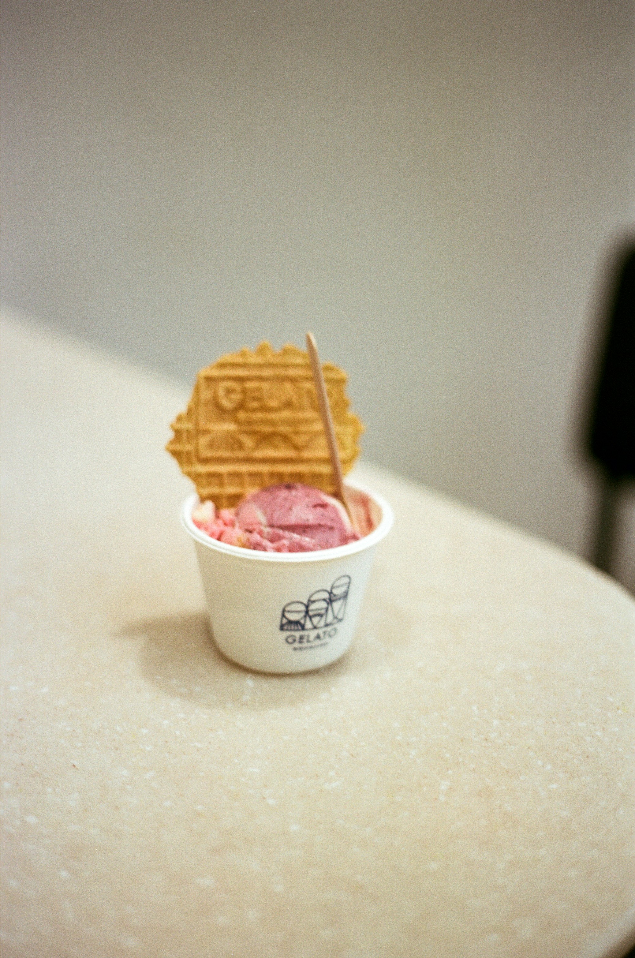 A scoop of pink gelato in a paper cup with a wafer cookie