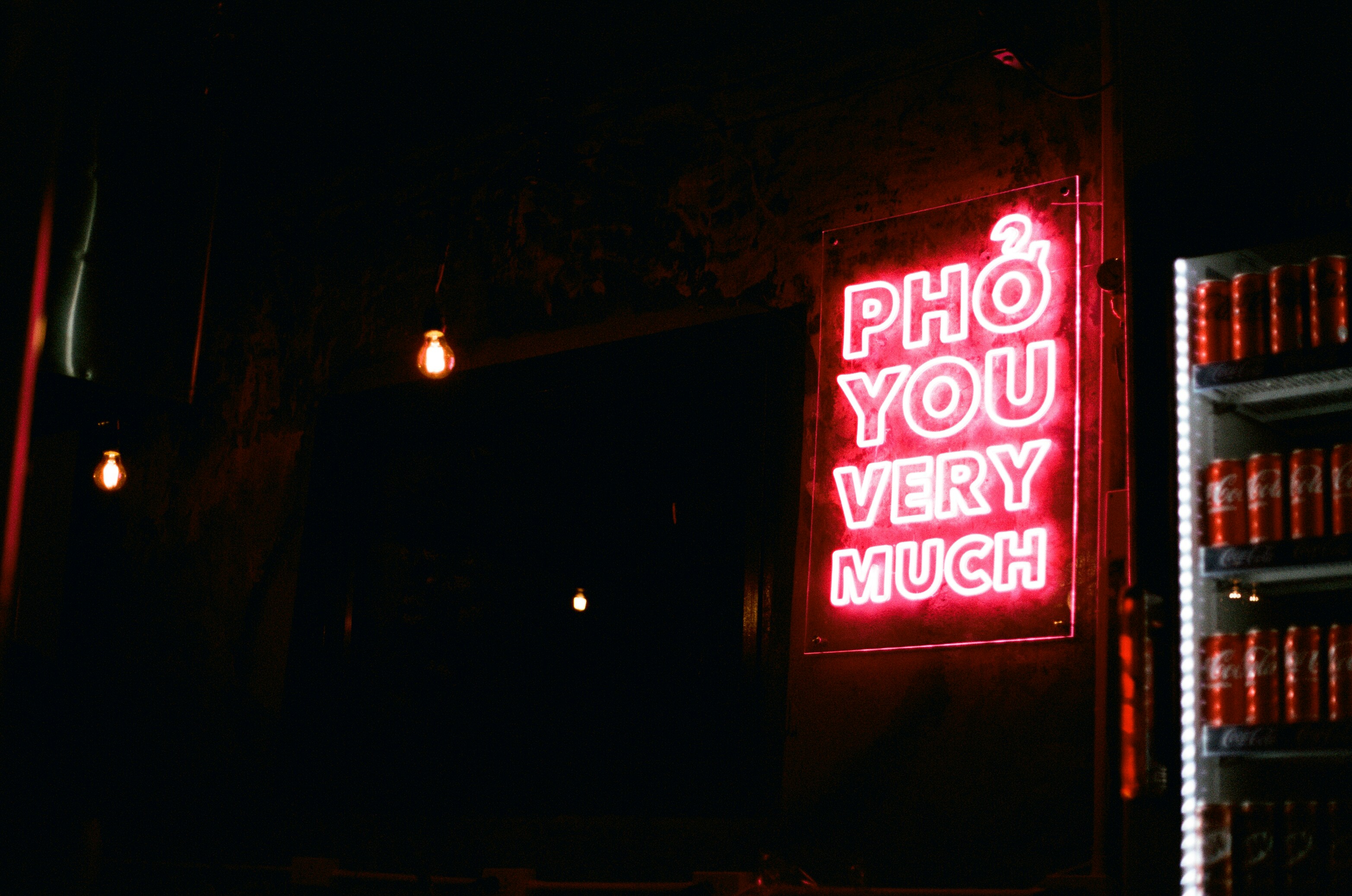 A bright red neon sign reading "PHO YOU VERY MUCH" on a dark wall