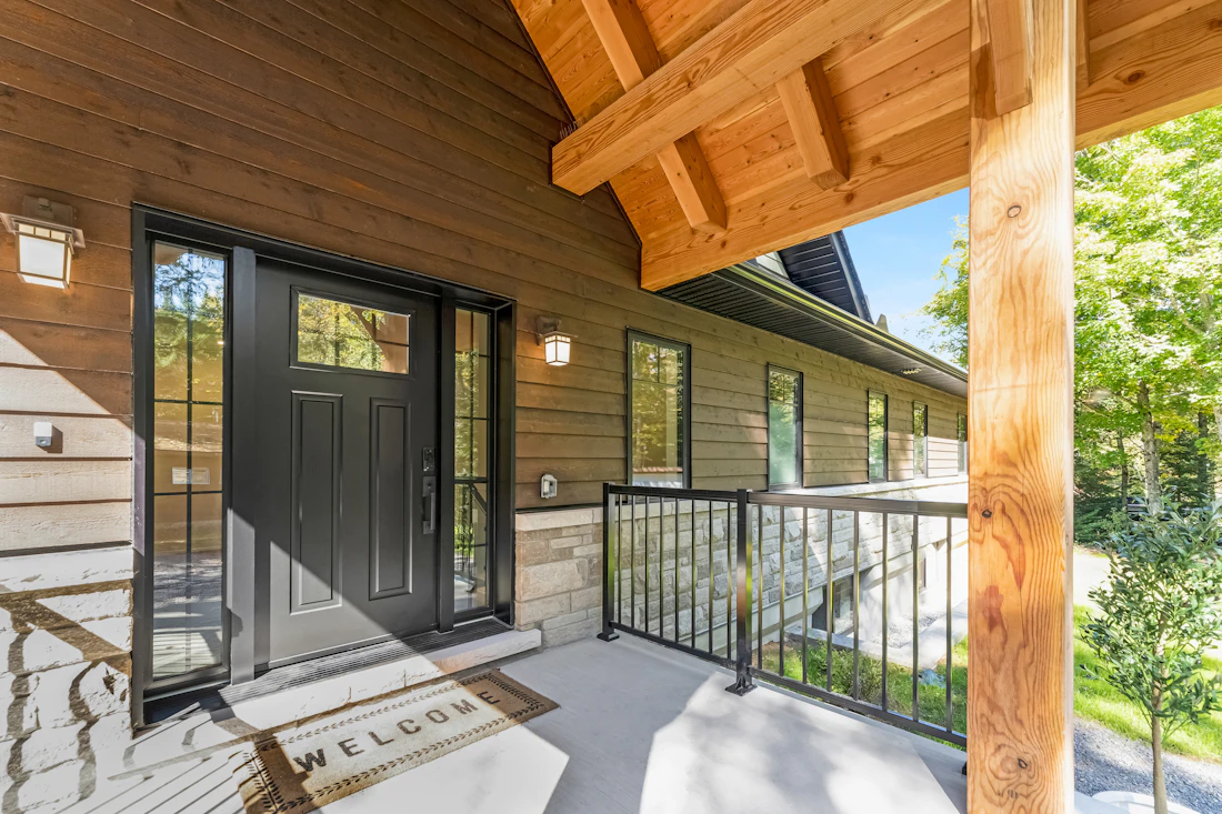 Black front door with a welcome mat on a wooden porch
