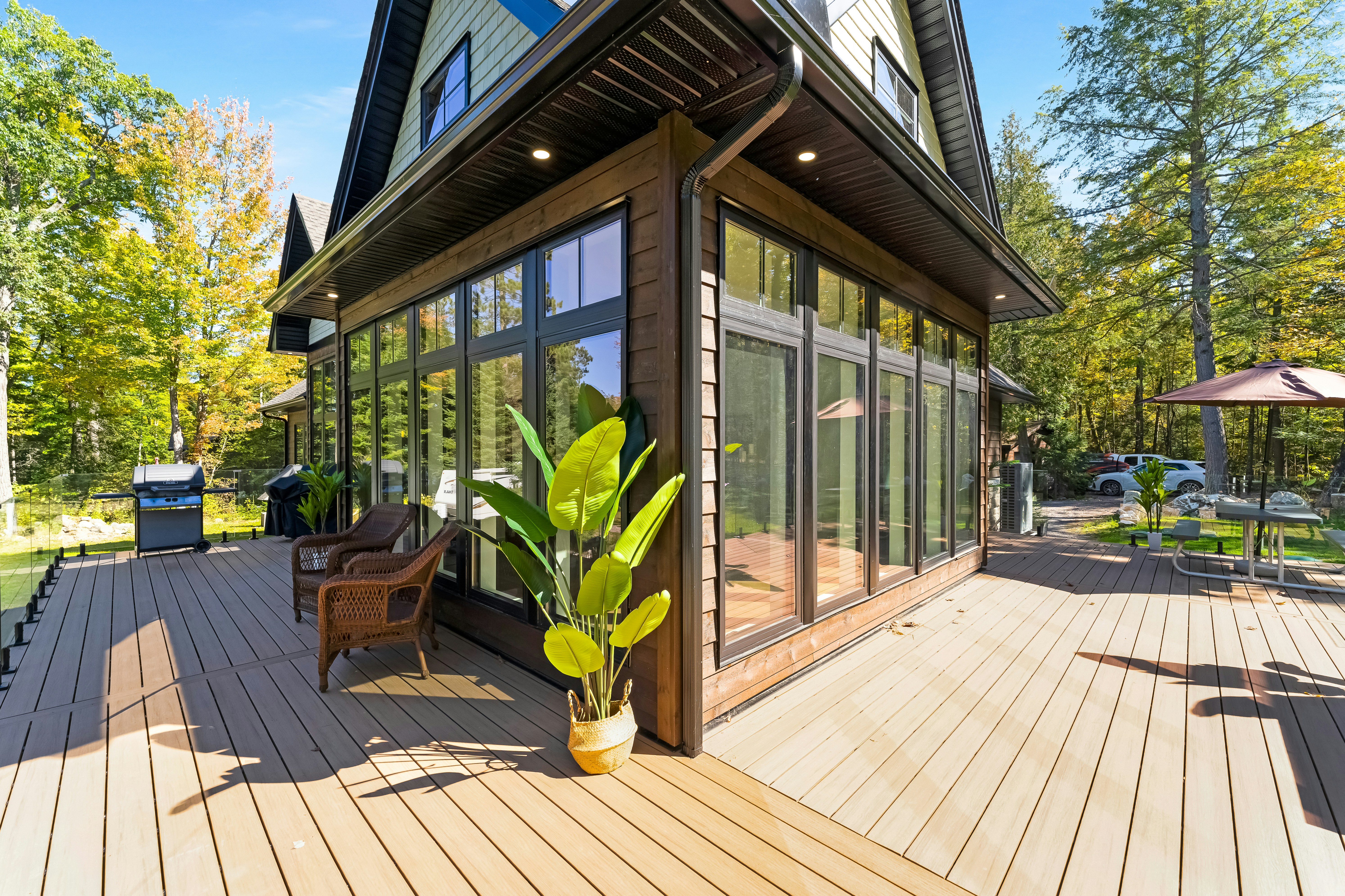 A glazed room with a timber deck and wicker chairs beside a house