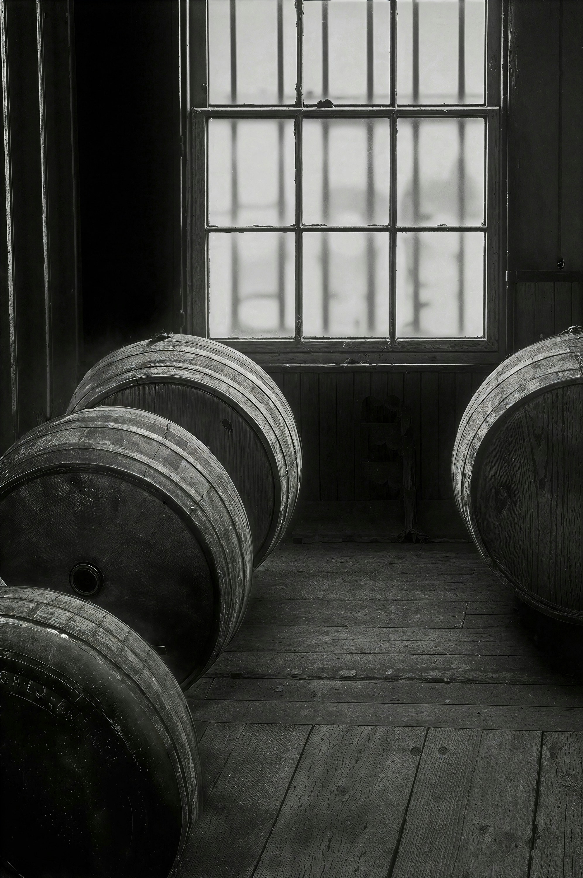 Three wooden barrels on a rustic floor in front of a window