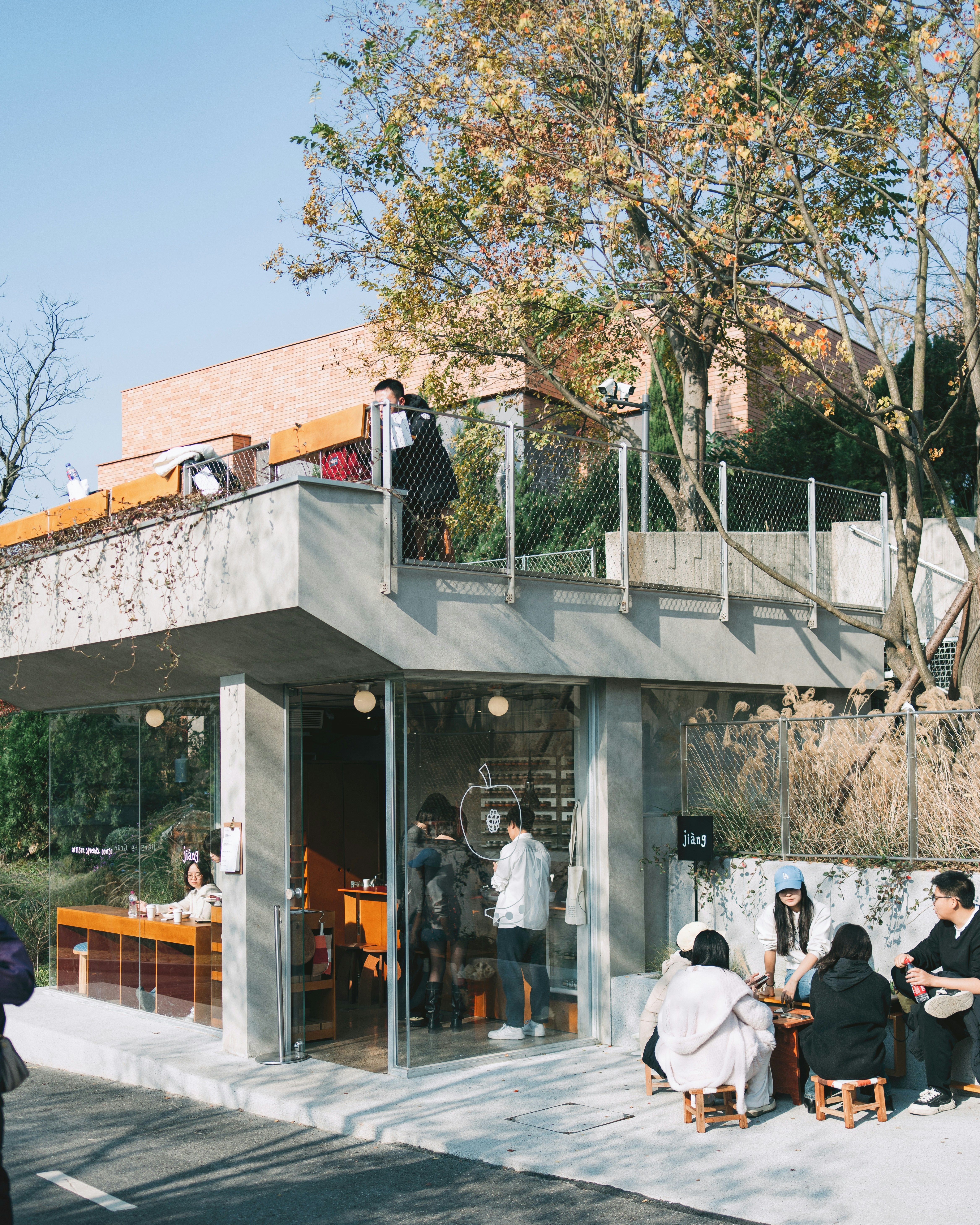 People sitting at a modern glass cafe with an outdoor terrace and trees