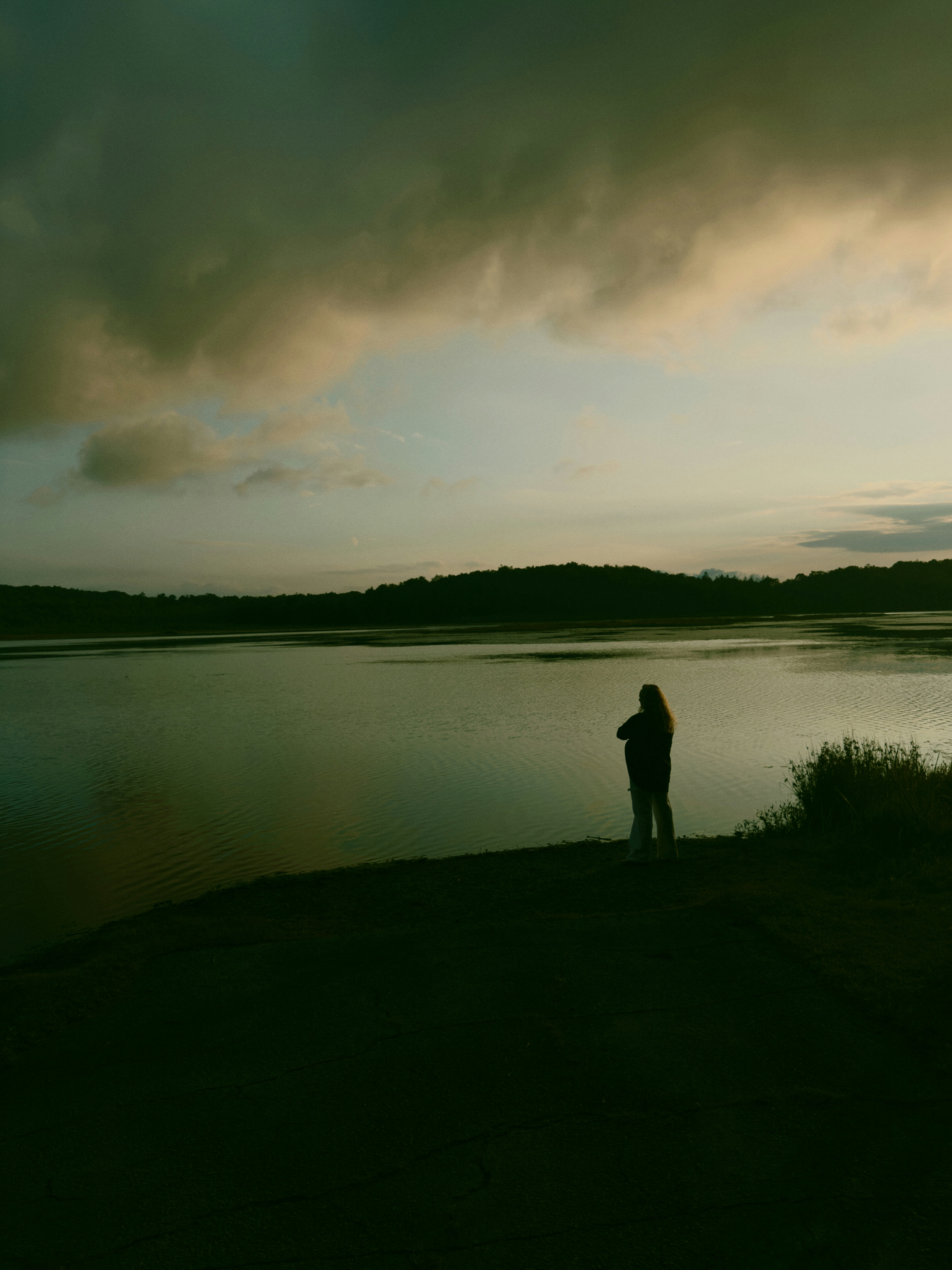 A person in silhouette on a lakeshore under a cloudy sky