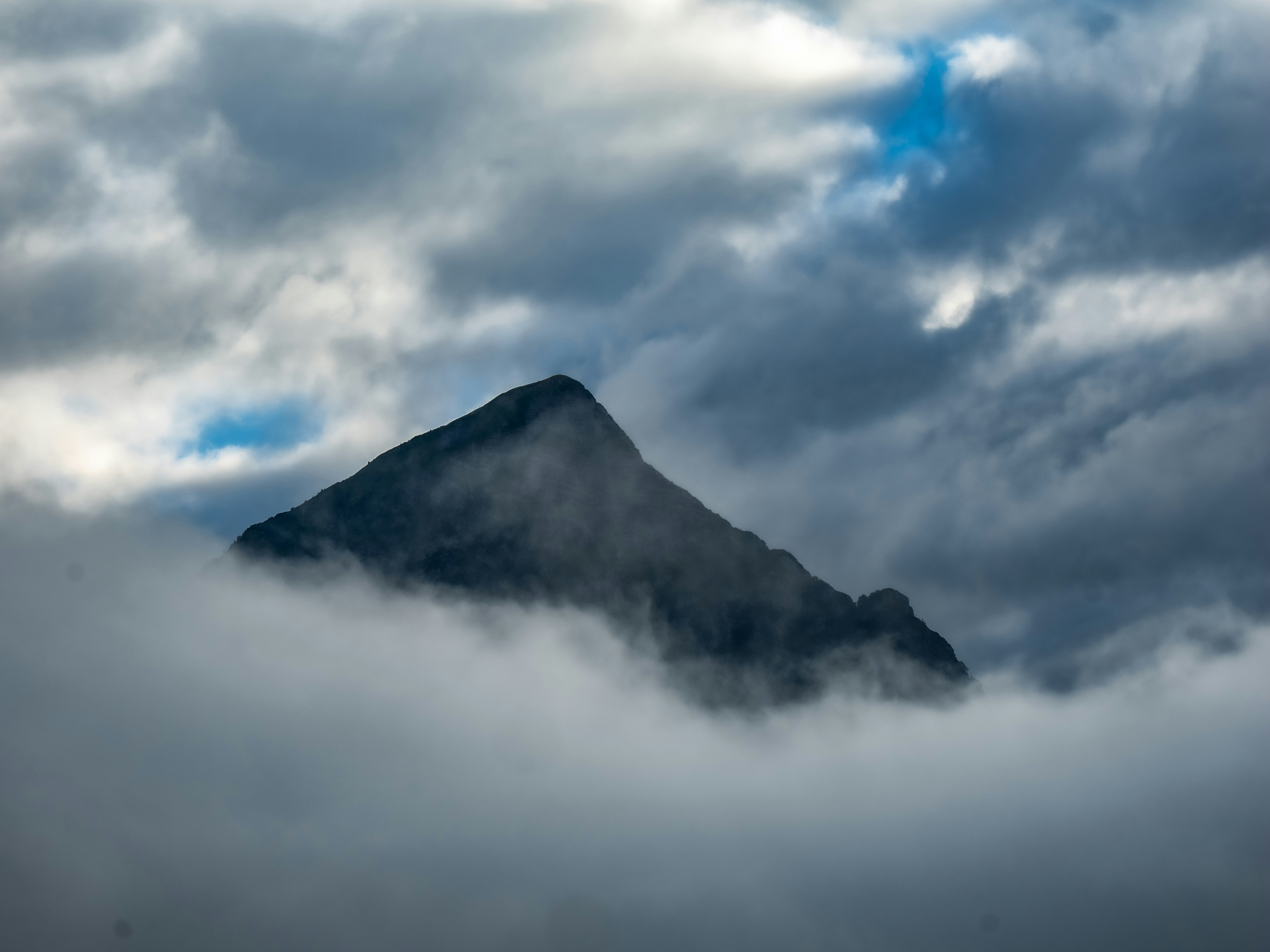 A dark mountain peak rising above a thick layer of low clouds