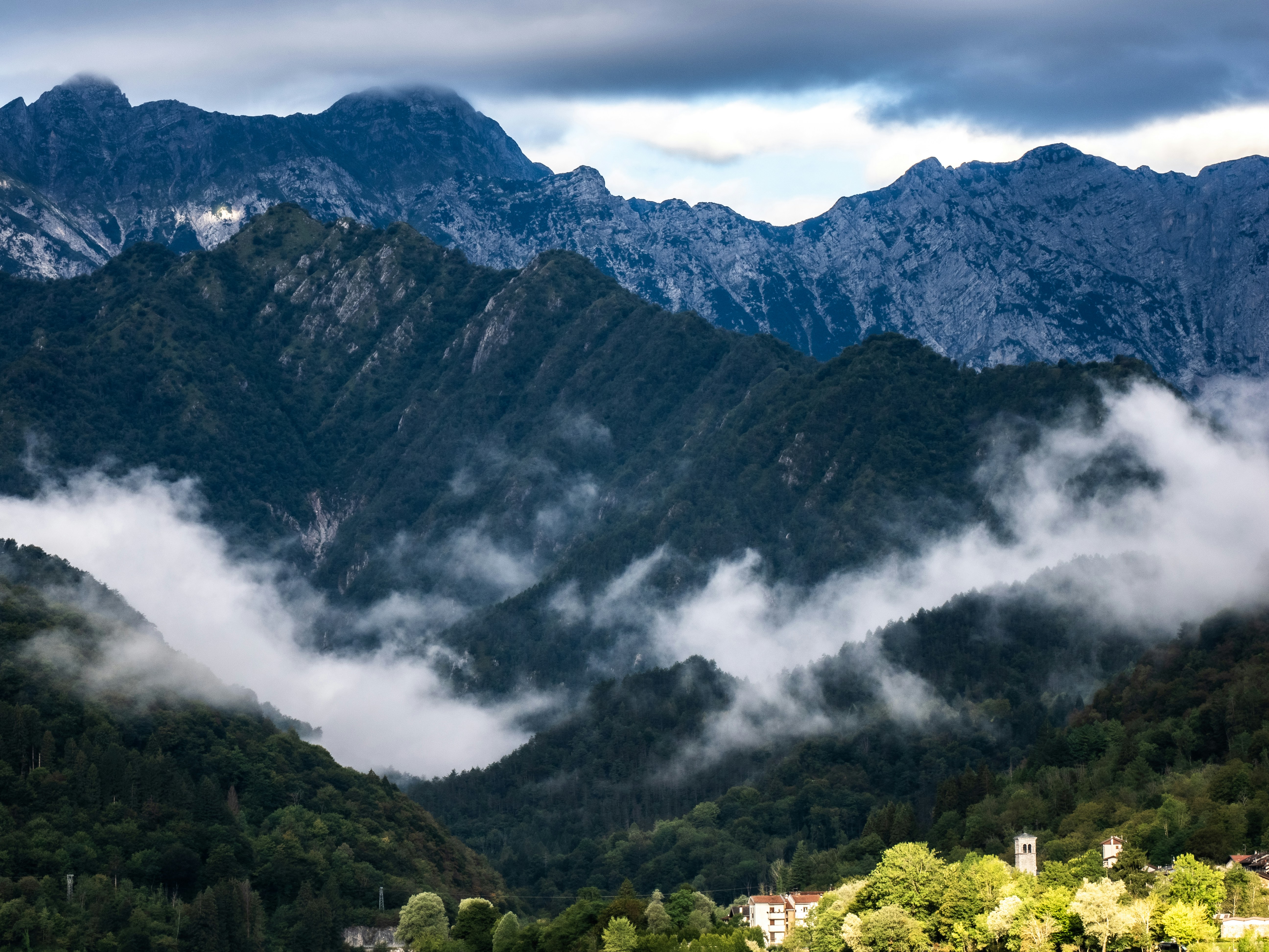 Low clouds drifting through a deep valley beneath jagged, dark mountain peaks