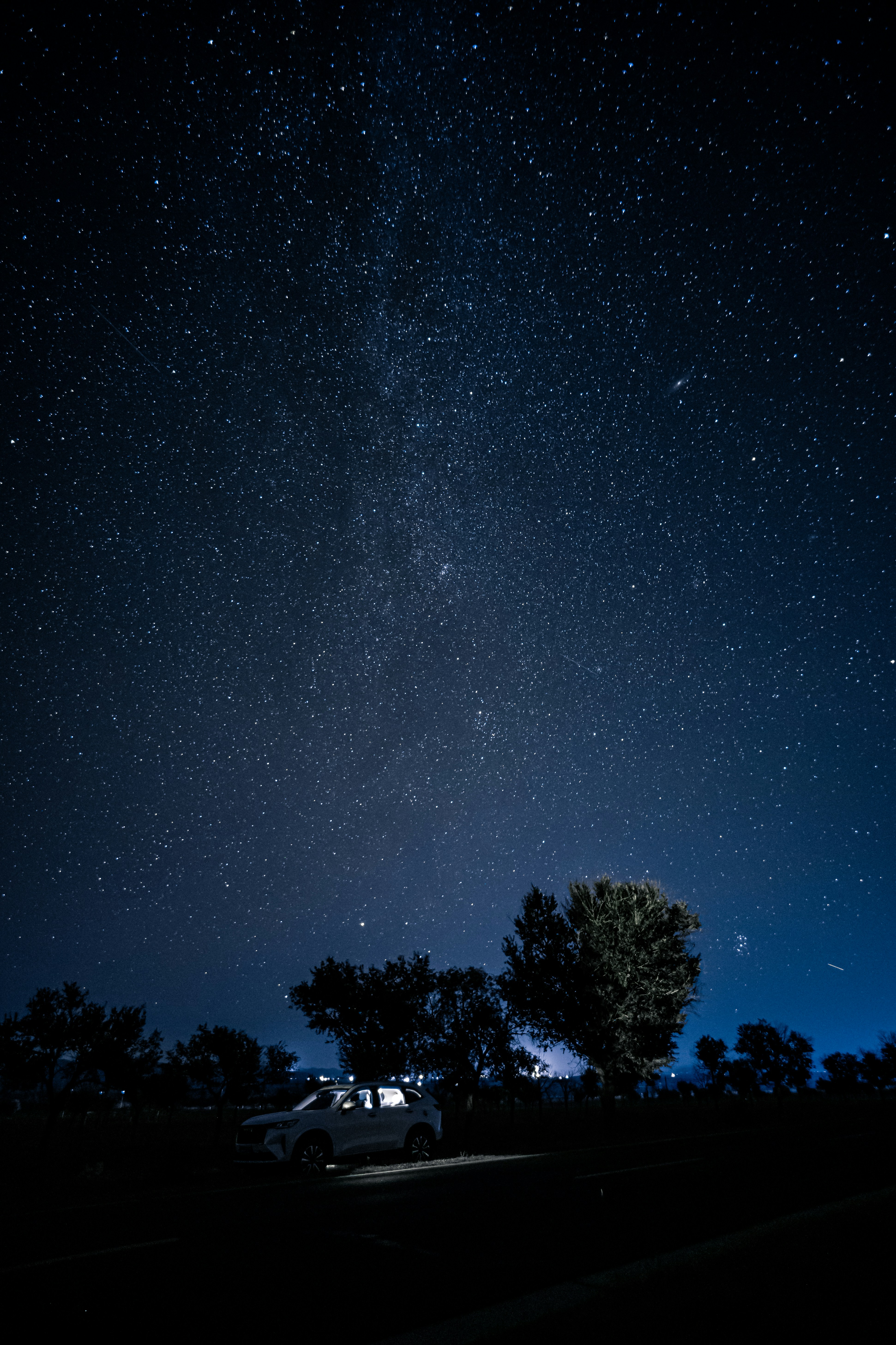 Un'auto bianca parcheggiata sotto un vasto cielo notturno pieno di stelle luminose