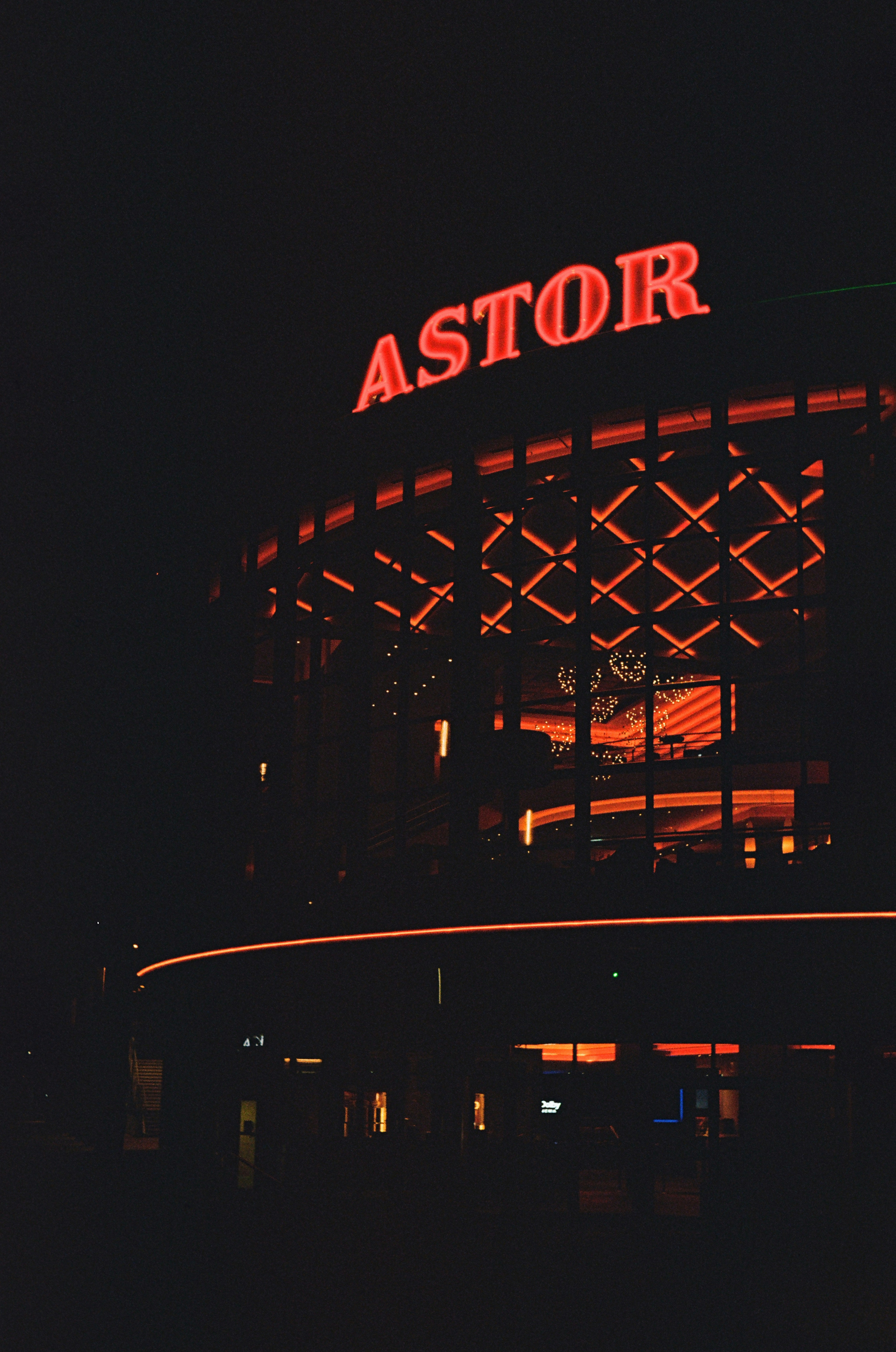 Fasad bangunan dengan papan neon merah menyala bertuliskan ASTOR di malam hari
