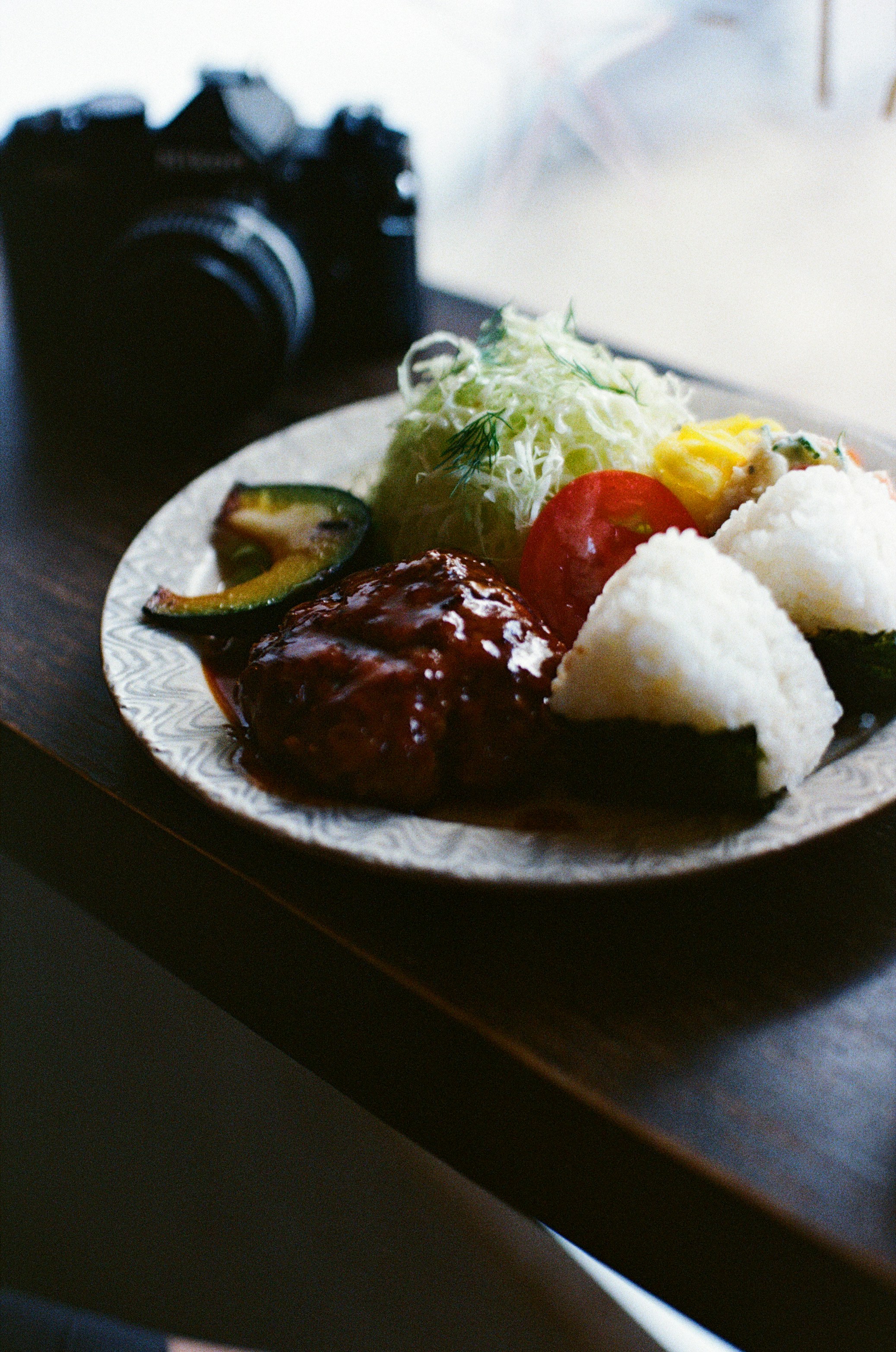 A plate with a hamburger steak, rice balls, and shredded cabbage