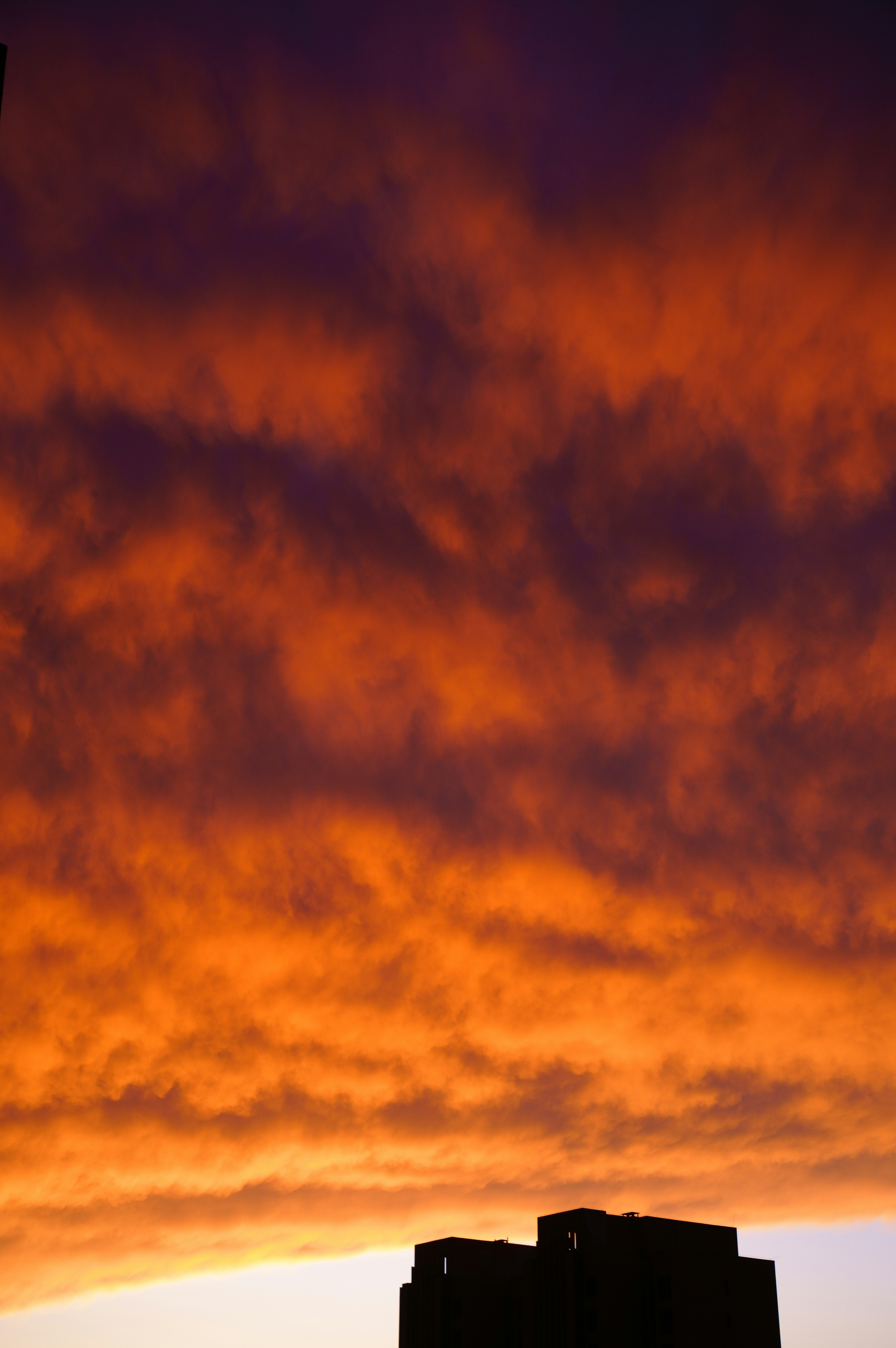 A dark building silhouette against a vibrant orange and purple cloudy sky