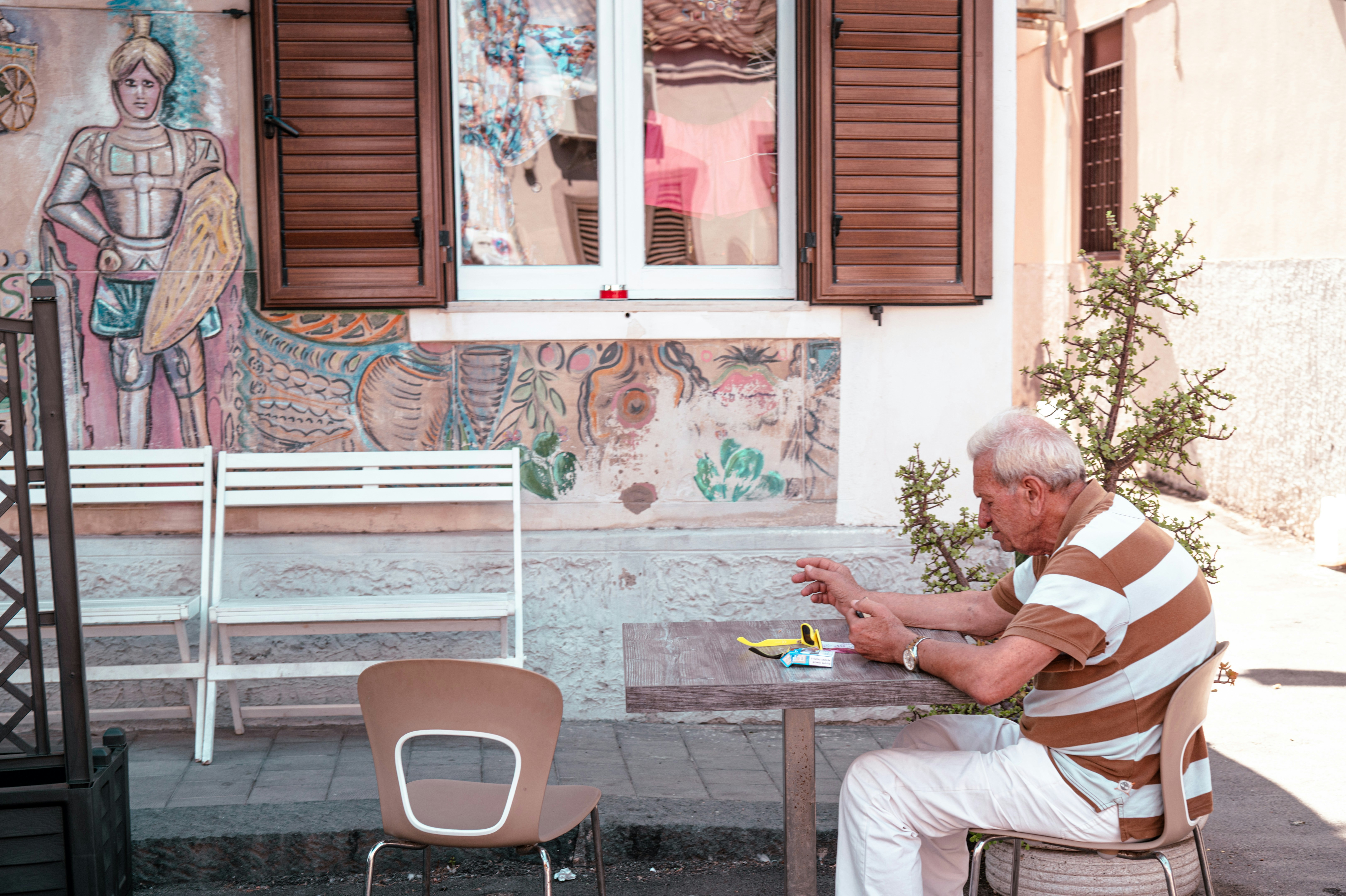 An elderly man in a striped shirt sitting at a table outdoors