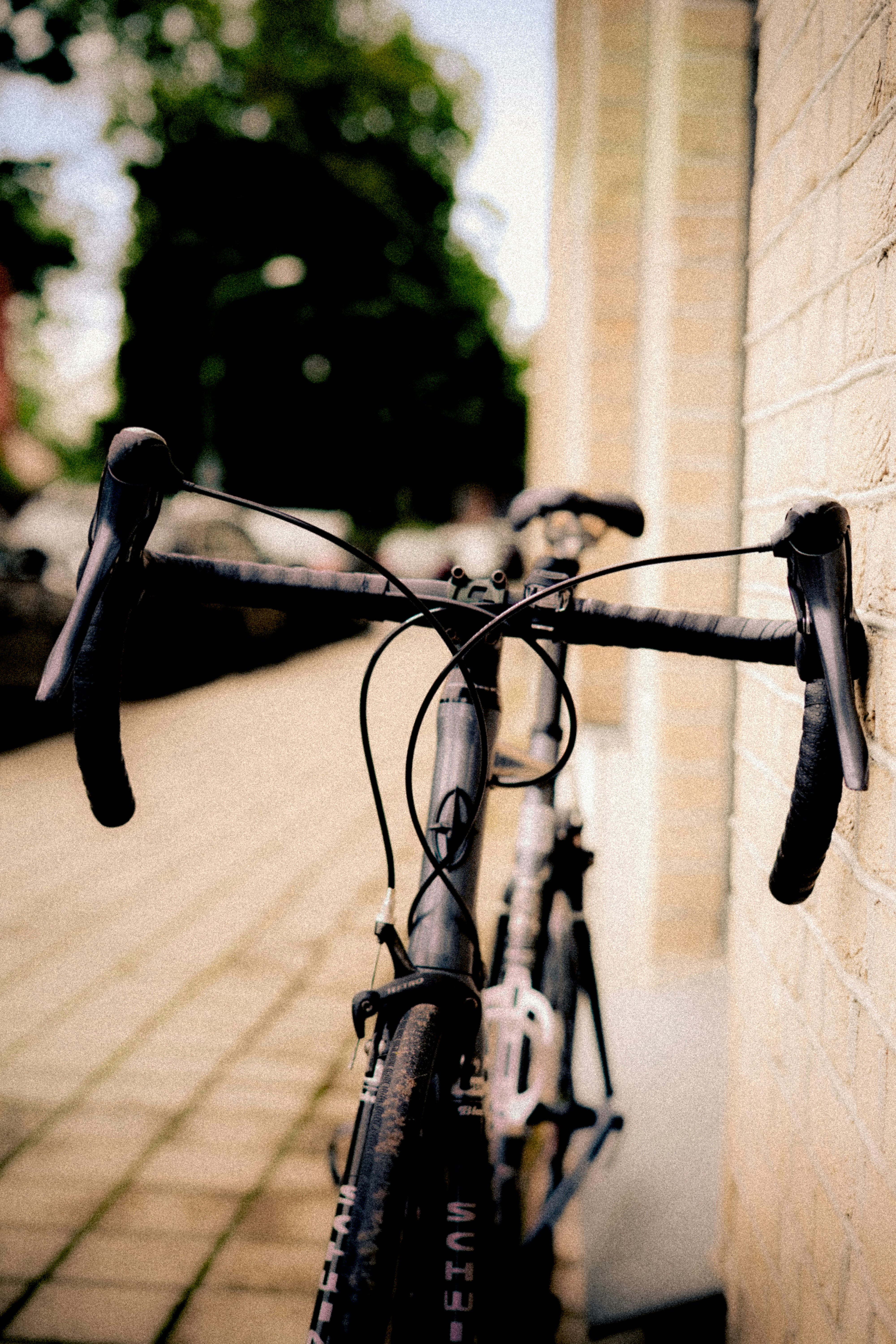 A black road bike leaning against a light brick wall on a sidewalk