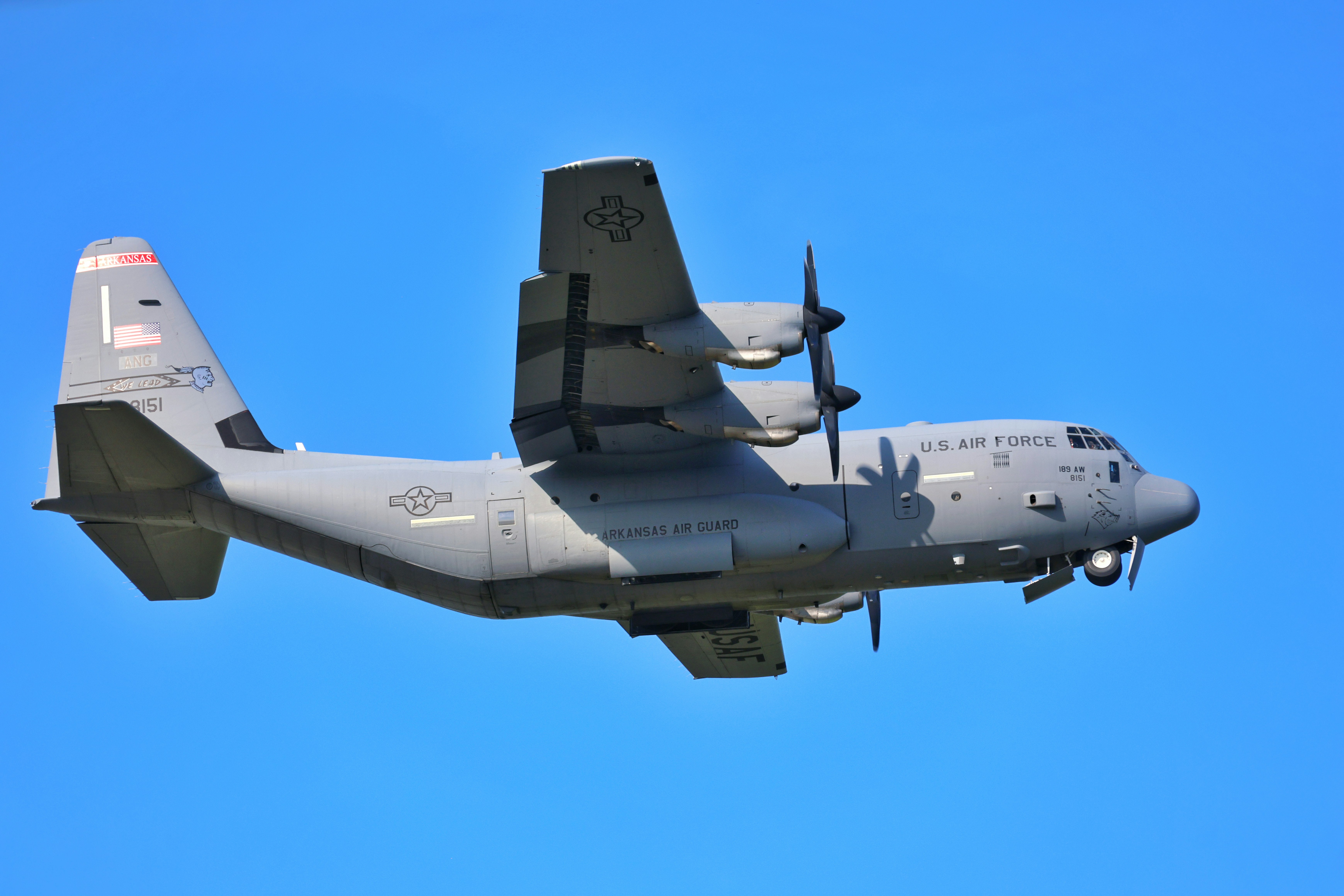 Ein graues C-130 Hercules Militärtransportflugzeug fliegt gegen einen klarblauen Himmel