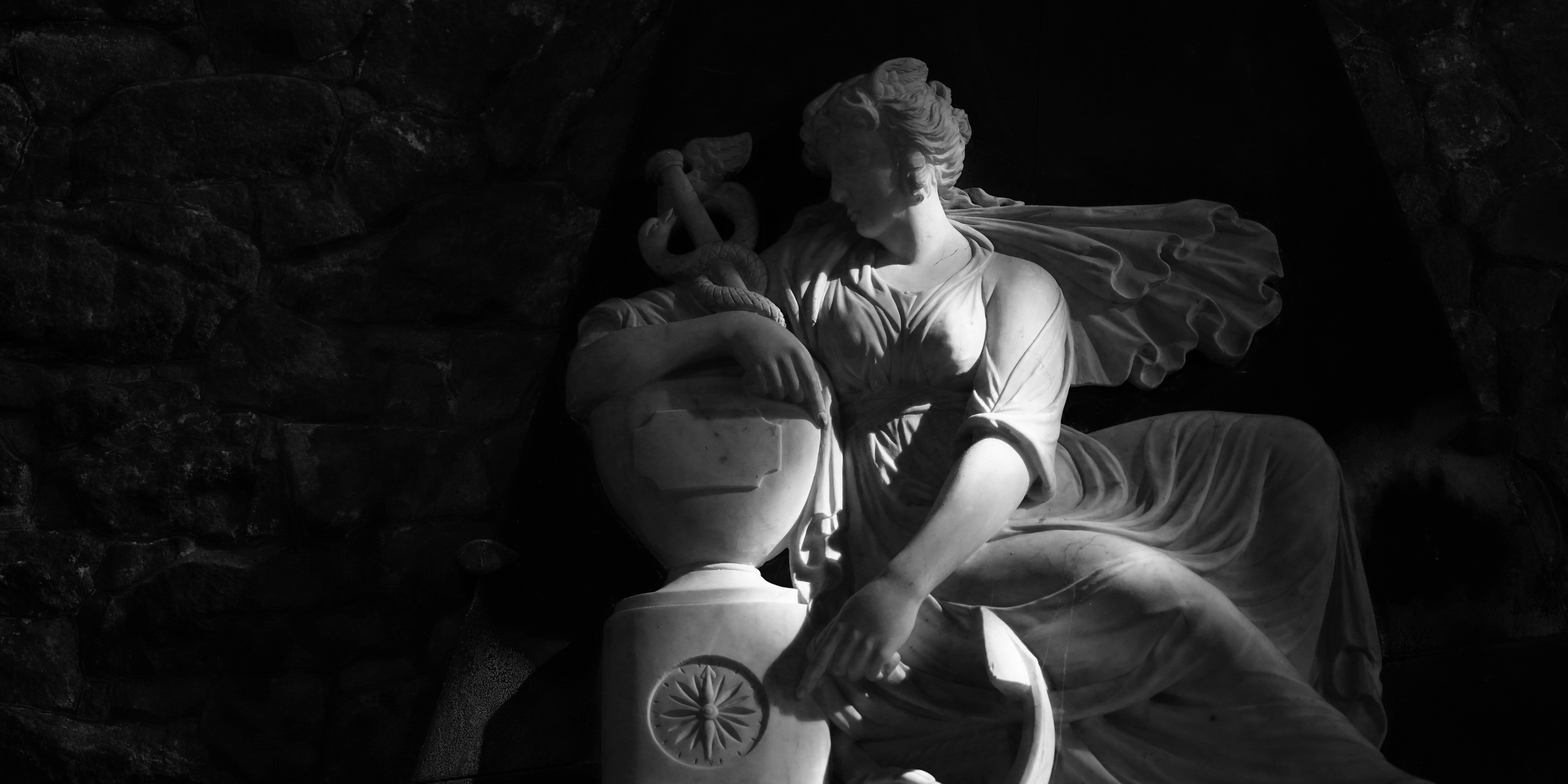 Uma estátua de mármore de uma mulher encostada em um pedestal com um caduceu