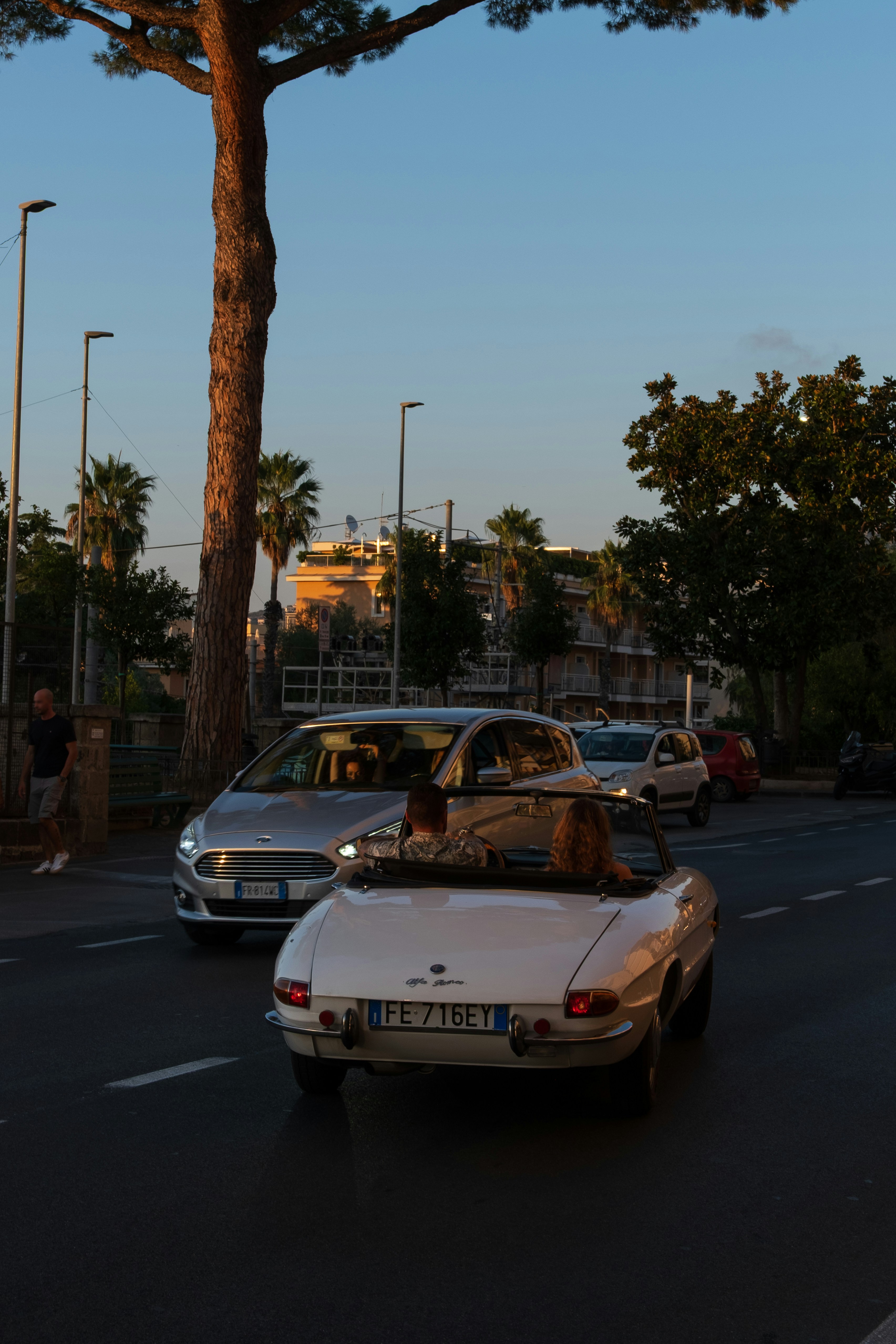 A white vintage Alfa Romeo convertible driving on a street at golden hour