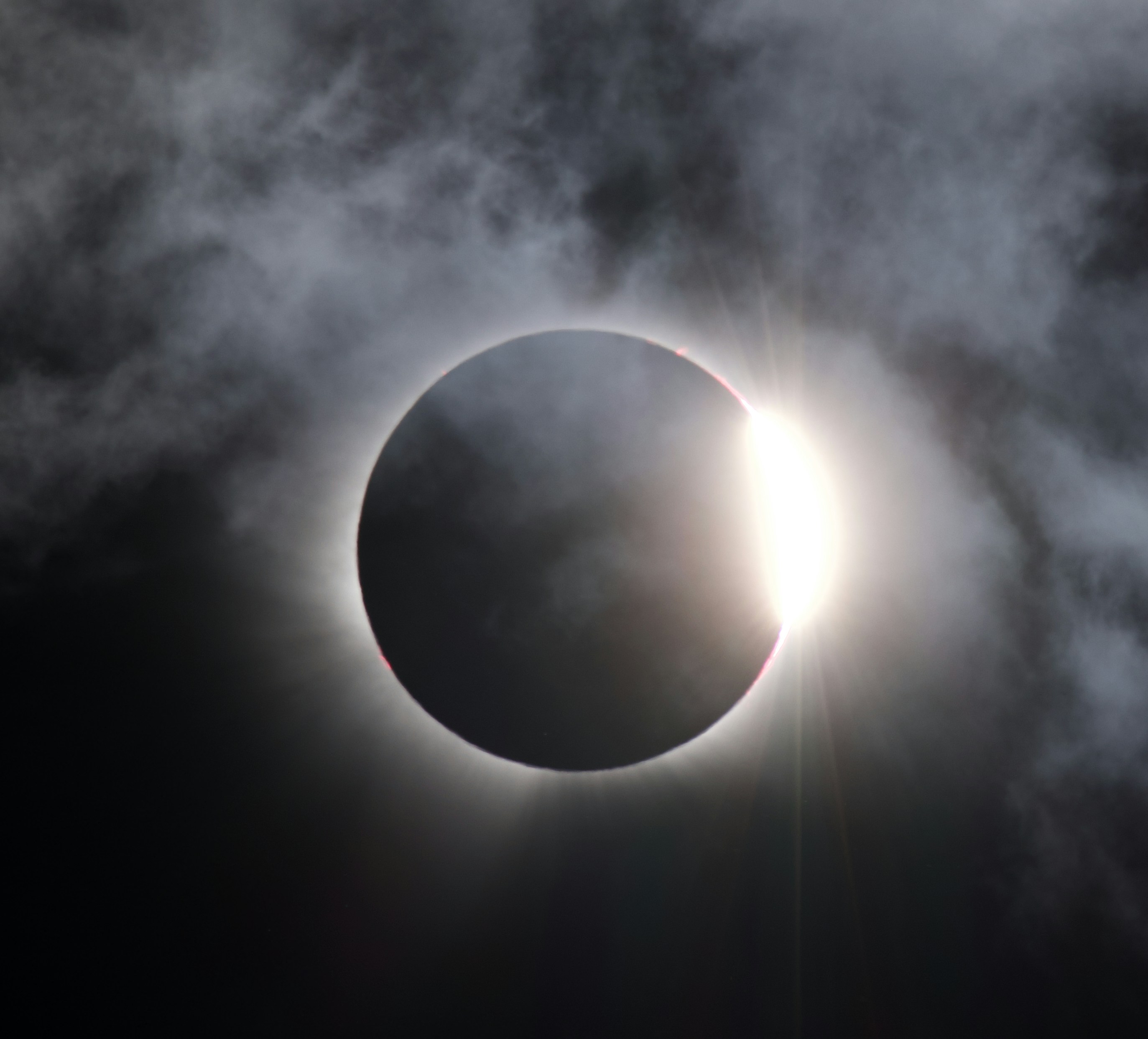 Eine totale Sonnenfinsternis mit einem hellen Lichtring hinter dunklen Wolken