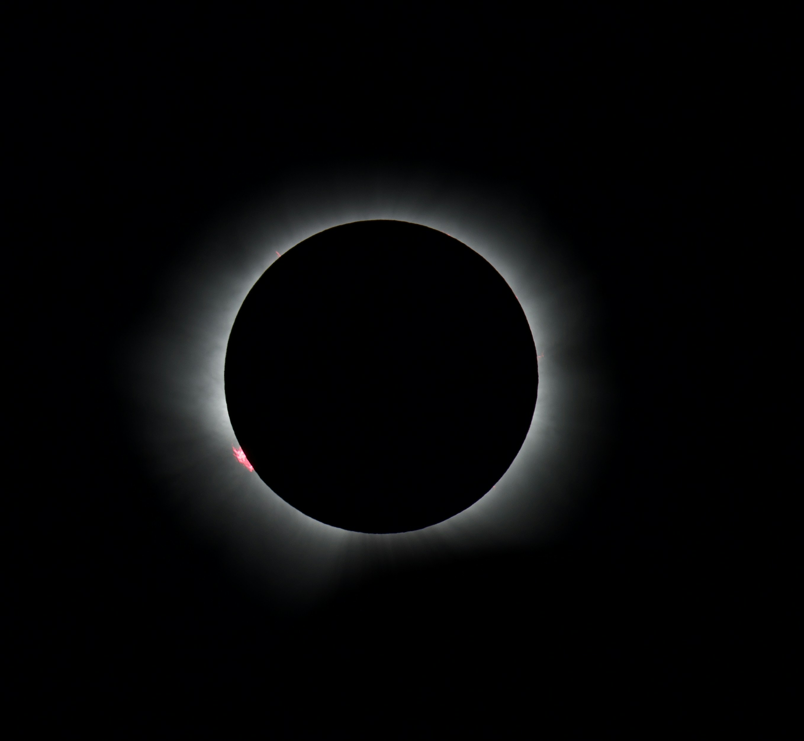 Eine totale Sonnenfinsternis mit einer leuchtenden Korona und roten Sonnenprominenzen