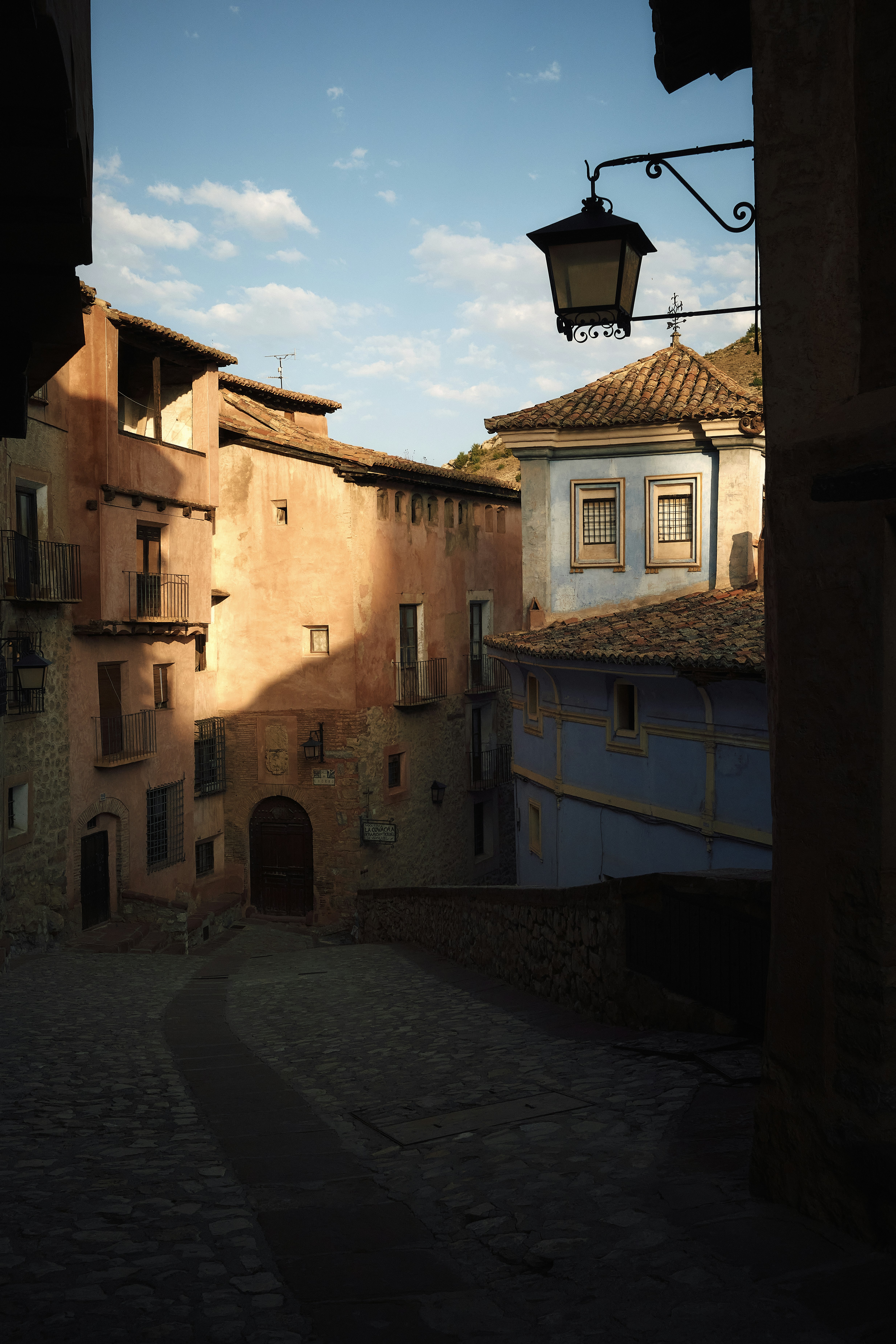 A cobblestone street between pink and blue buildings under a clear blue sky - 相关推荐