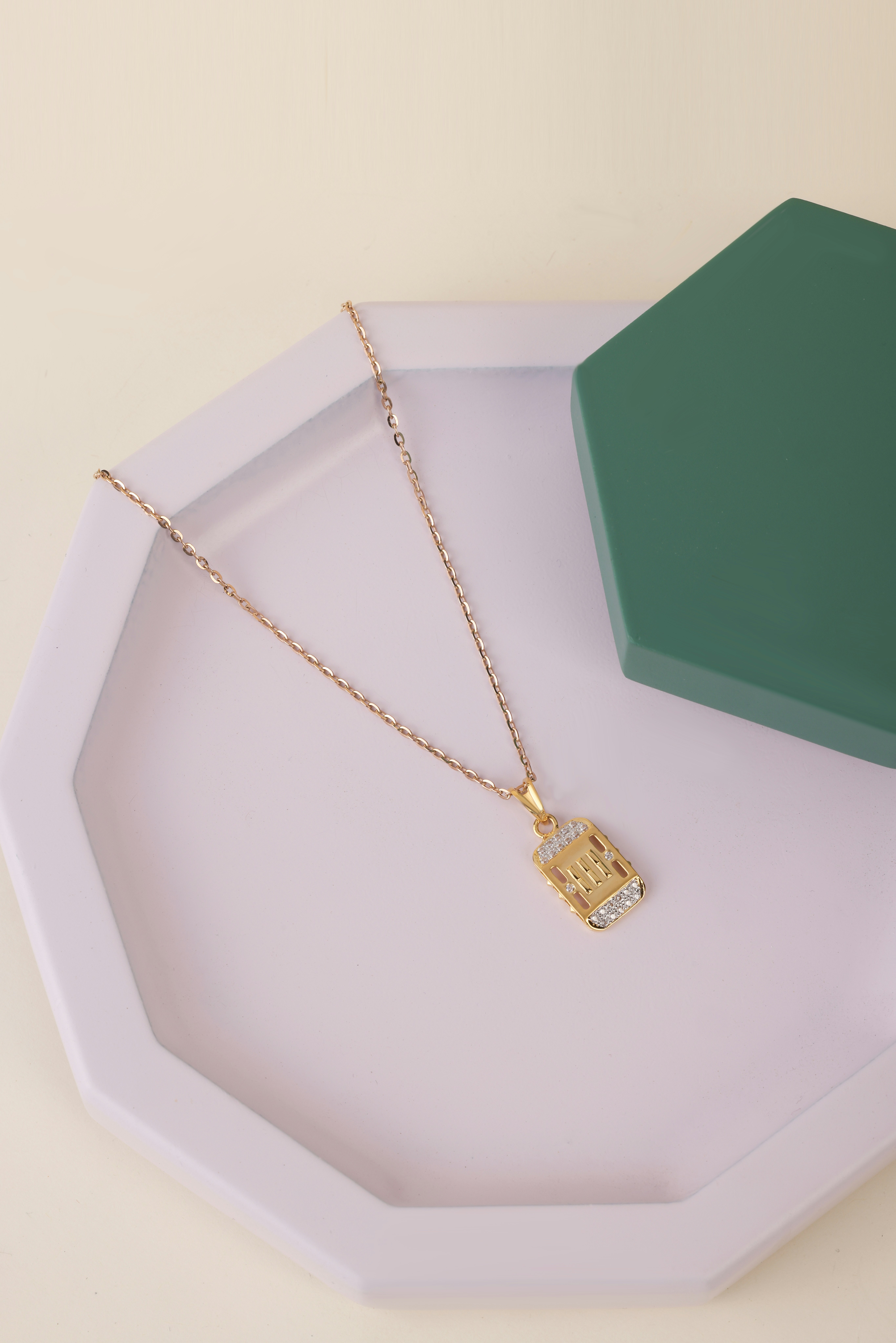 Kalung rantai emas dengan liontin persegi panjang di atas nampan ungu muda