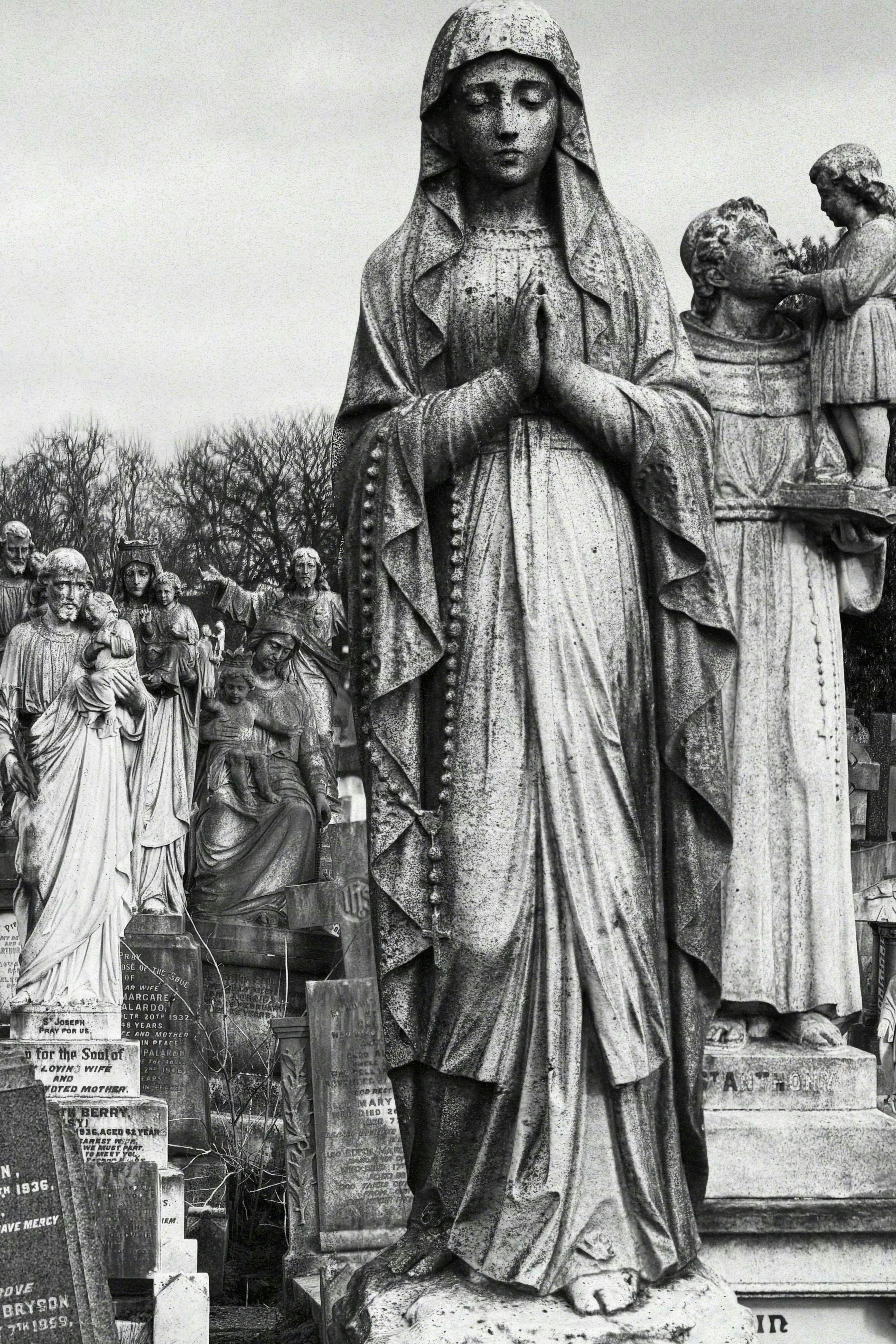 Stone statues of religious figures in a cemetery with weathered headstones