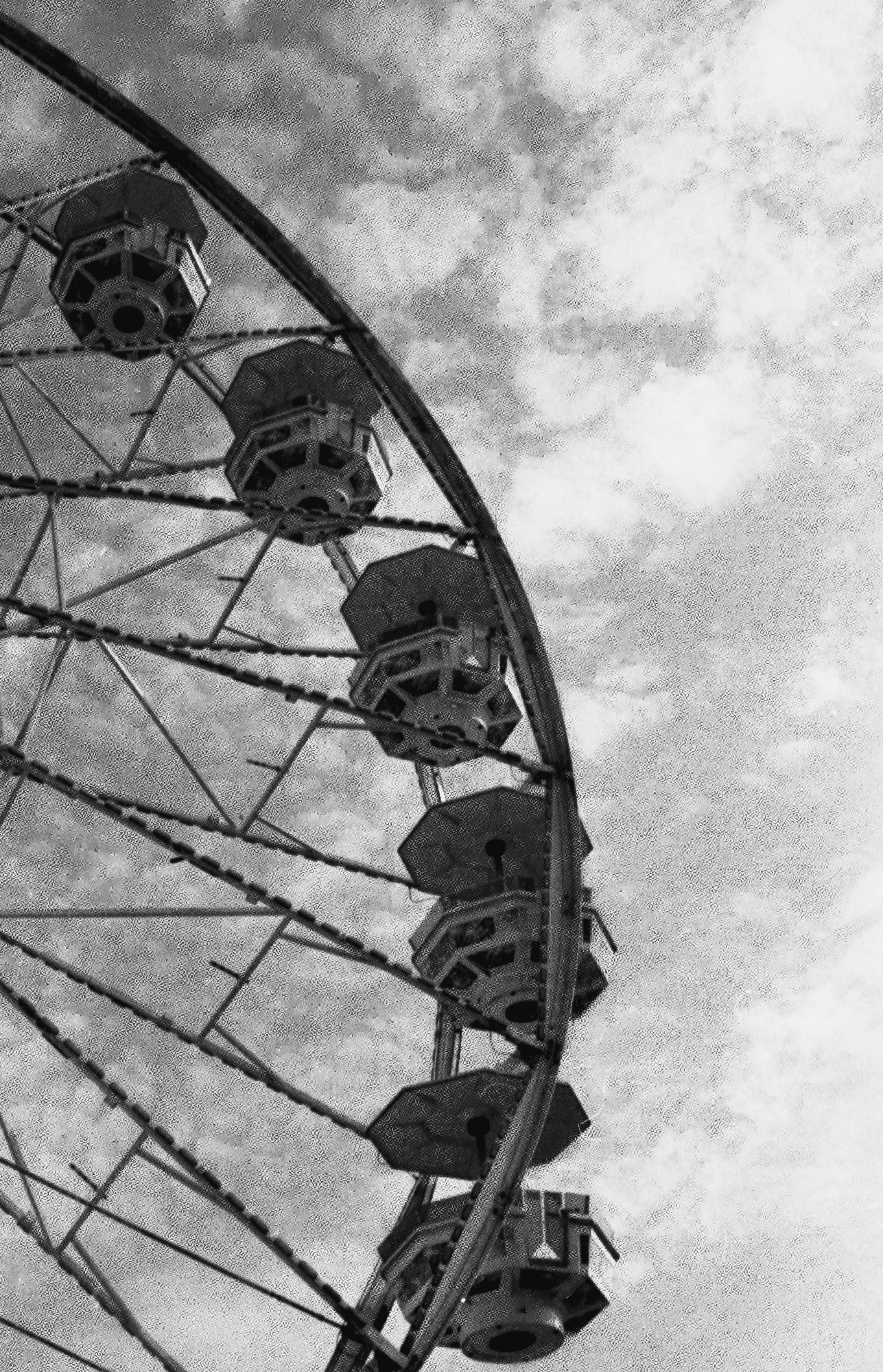 A black and white view of a ferris wheel against a cloudy sky
