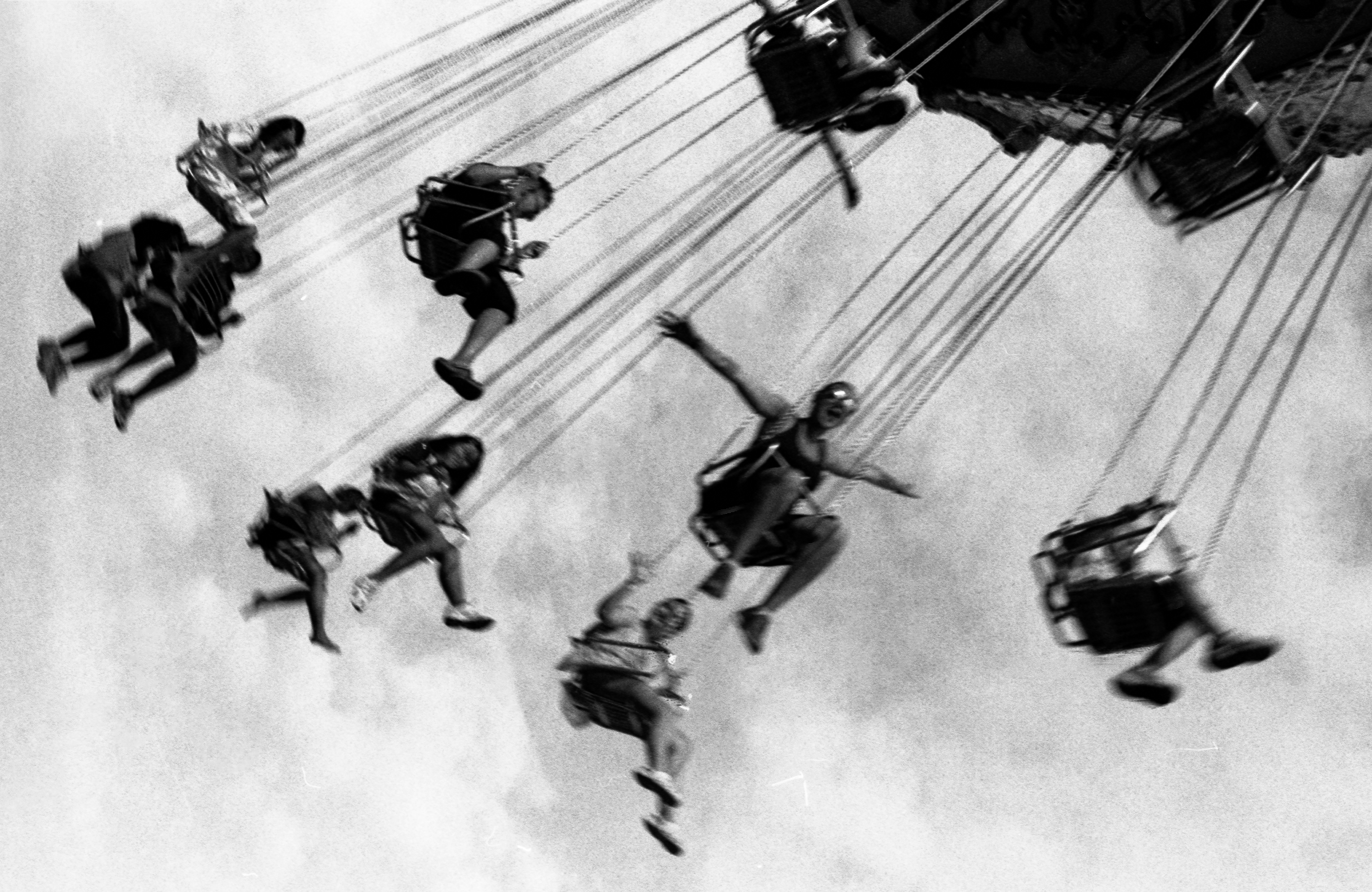 People in swings on a spinning carnival ride against a bright sky
