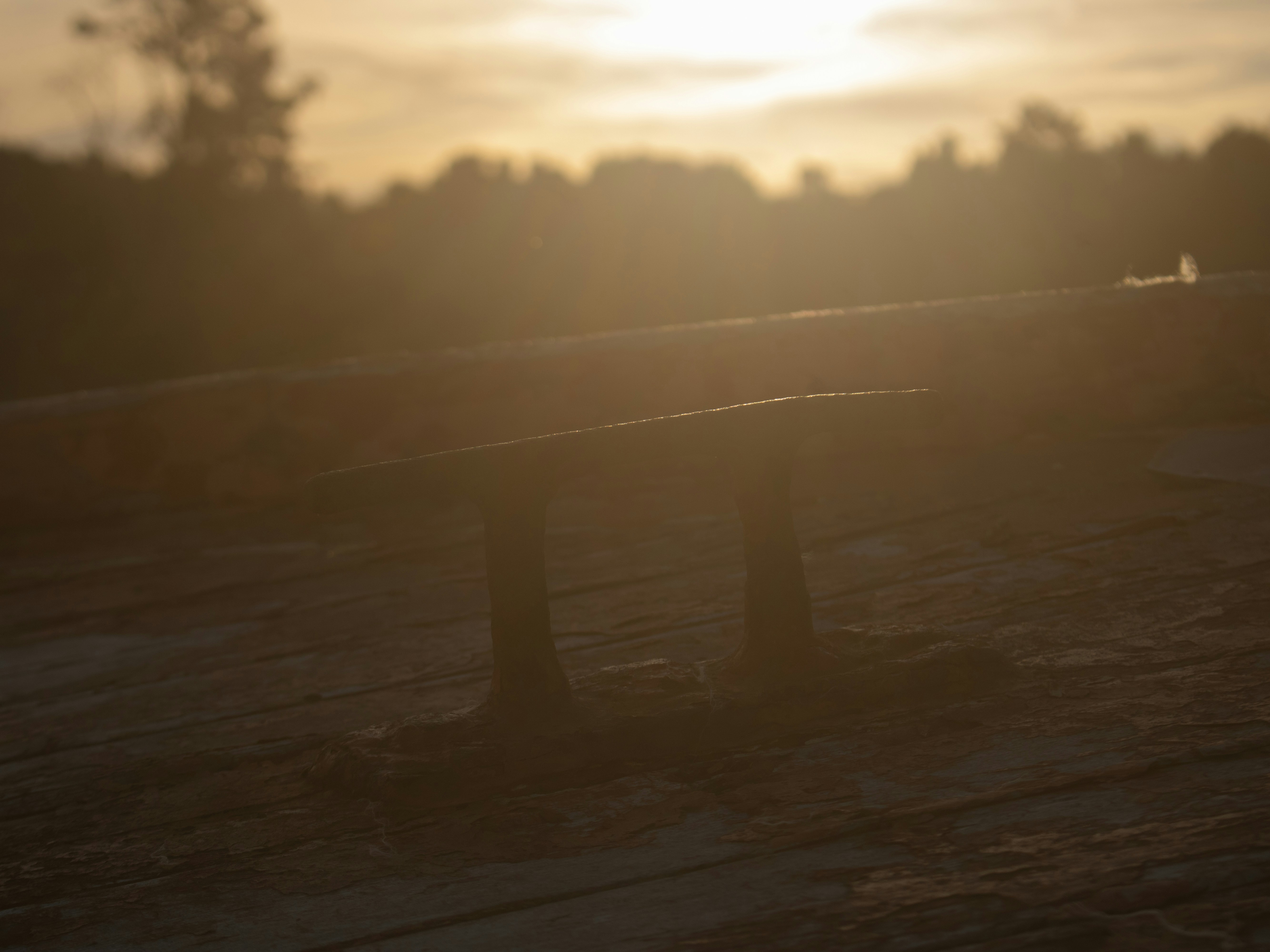 A metal boat cleat on a wooden deck during the golden hour