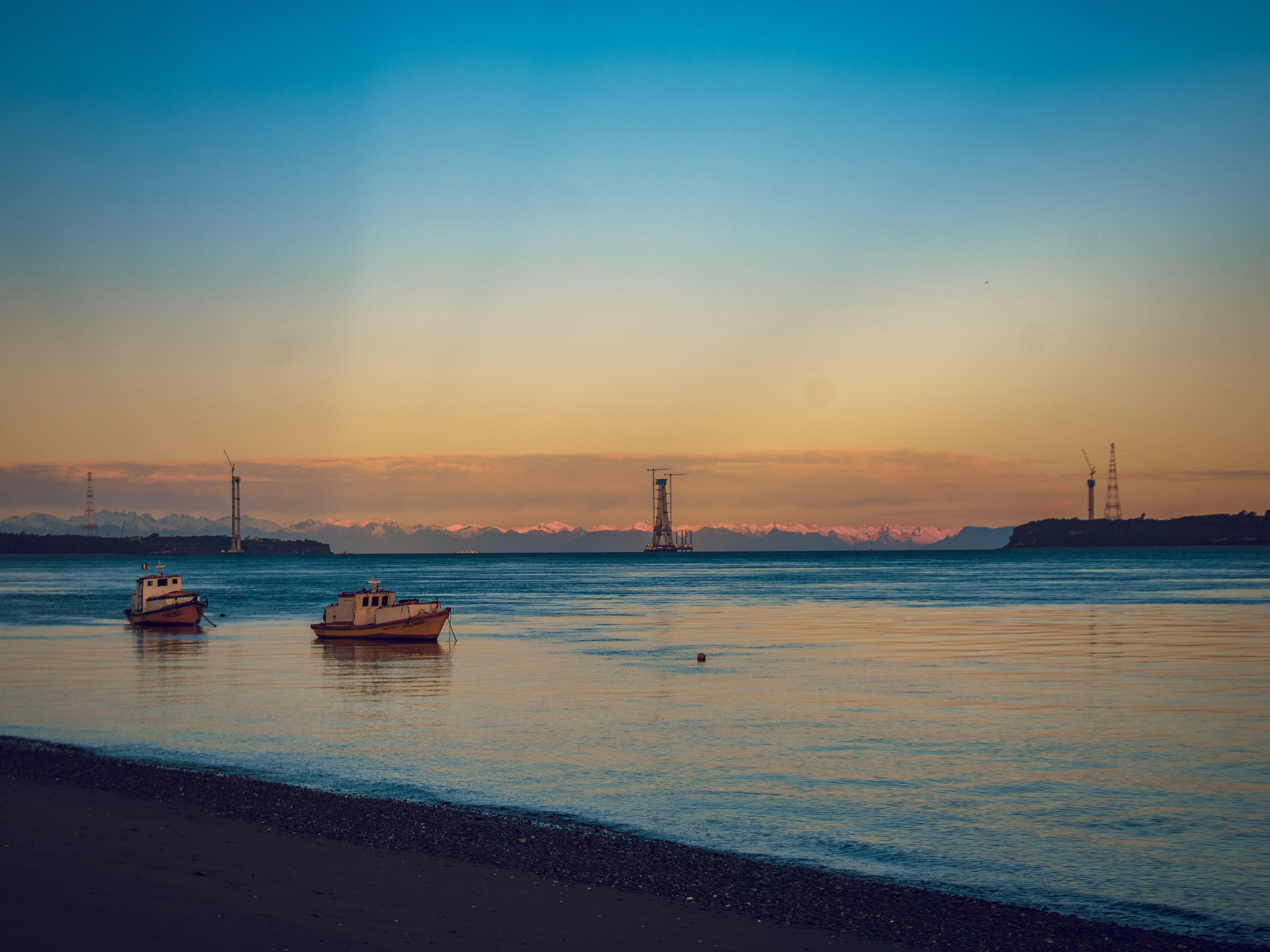 Two small boats anchored in calm water before a distant mountain range at golden hour
