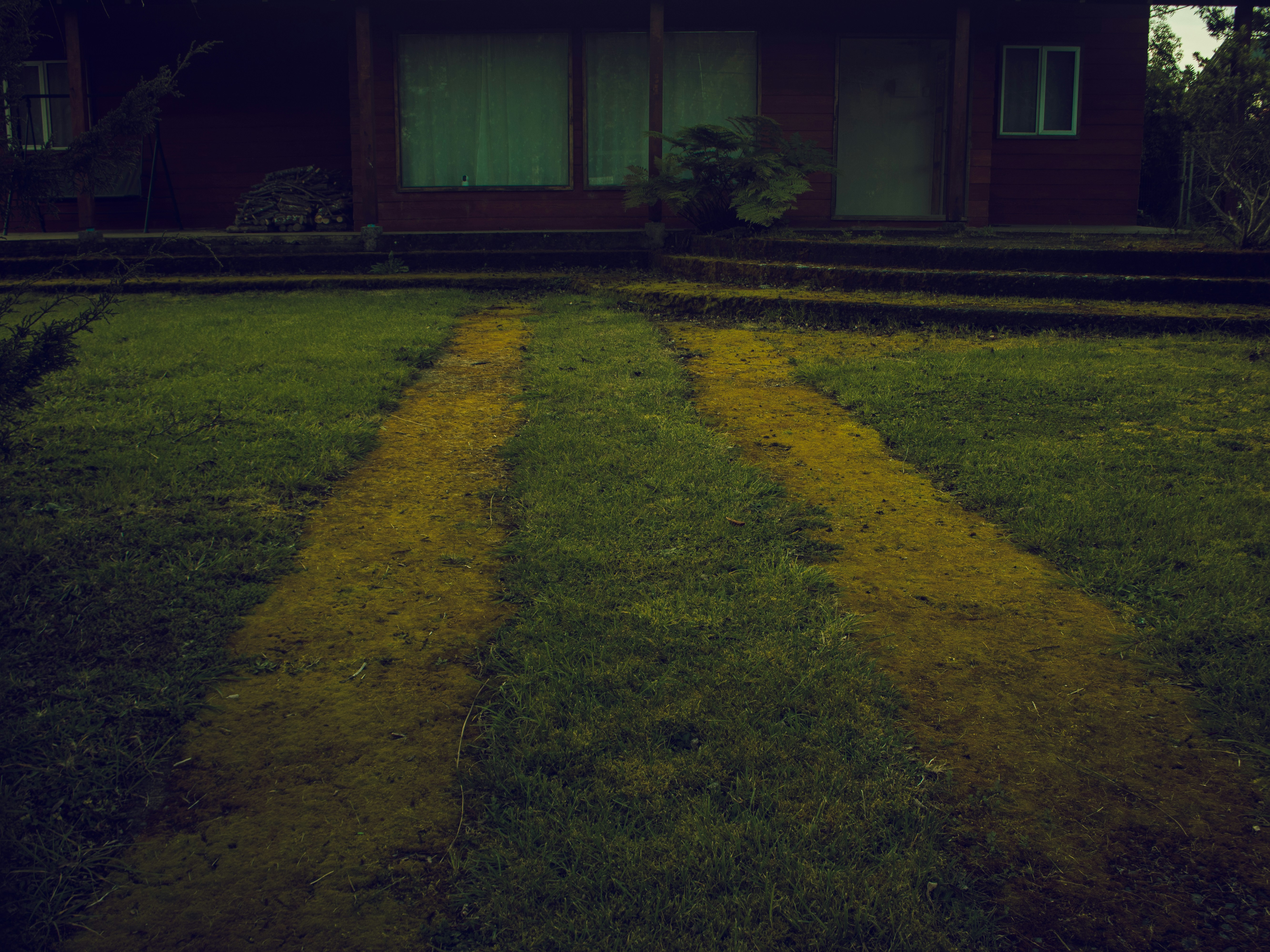 Two parallel dirt tracks through a grassy lawn leading to a dark wooden house