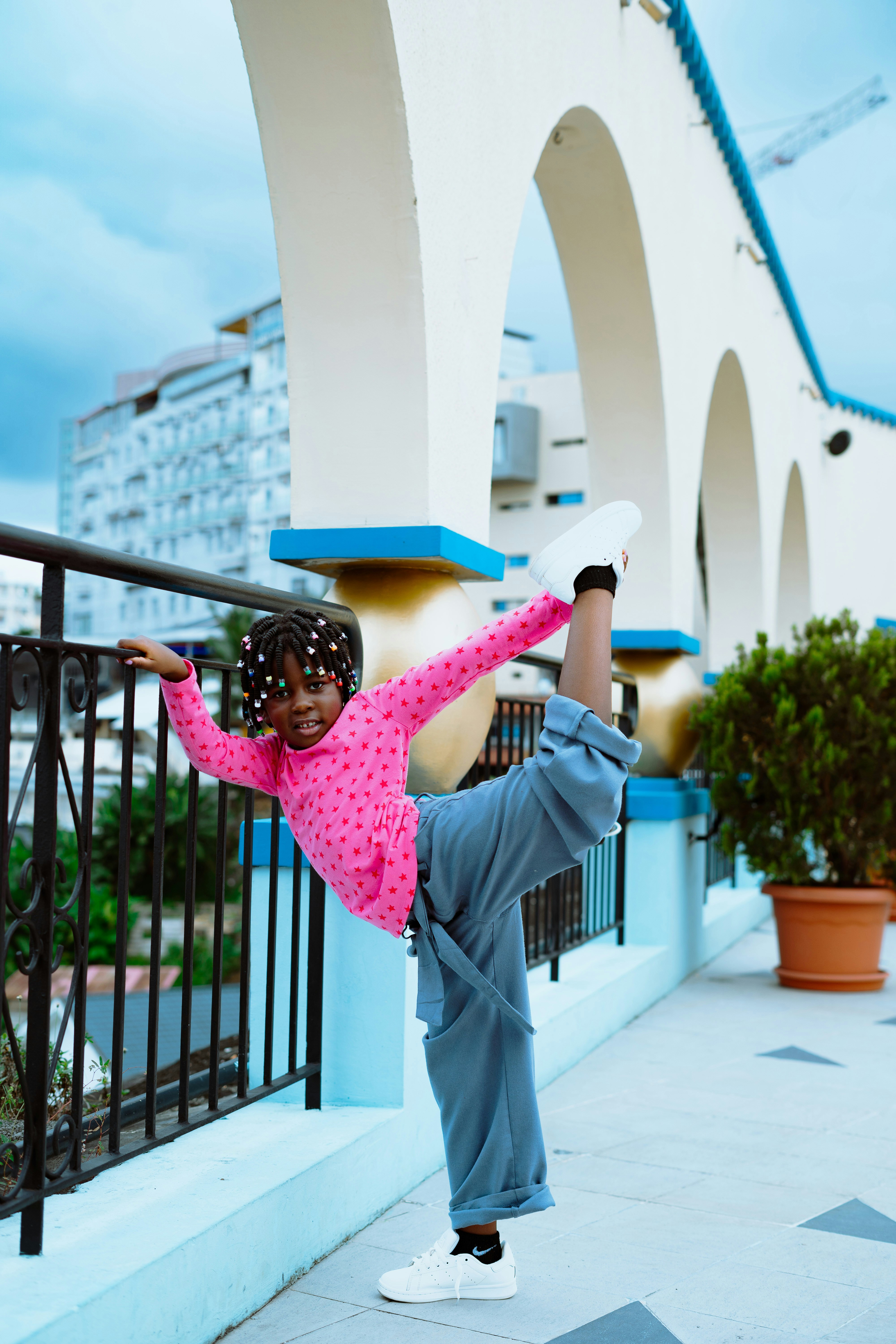 A child in a pink star-patterned shirt performing a standing leg hold on a balcony