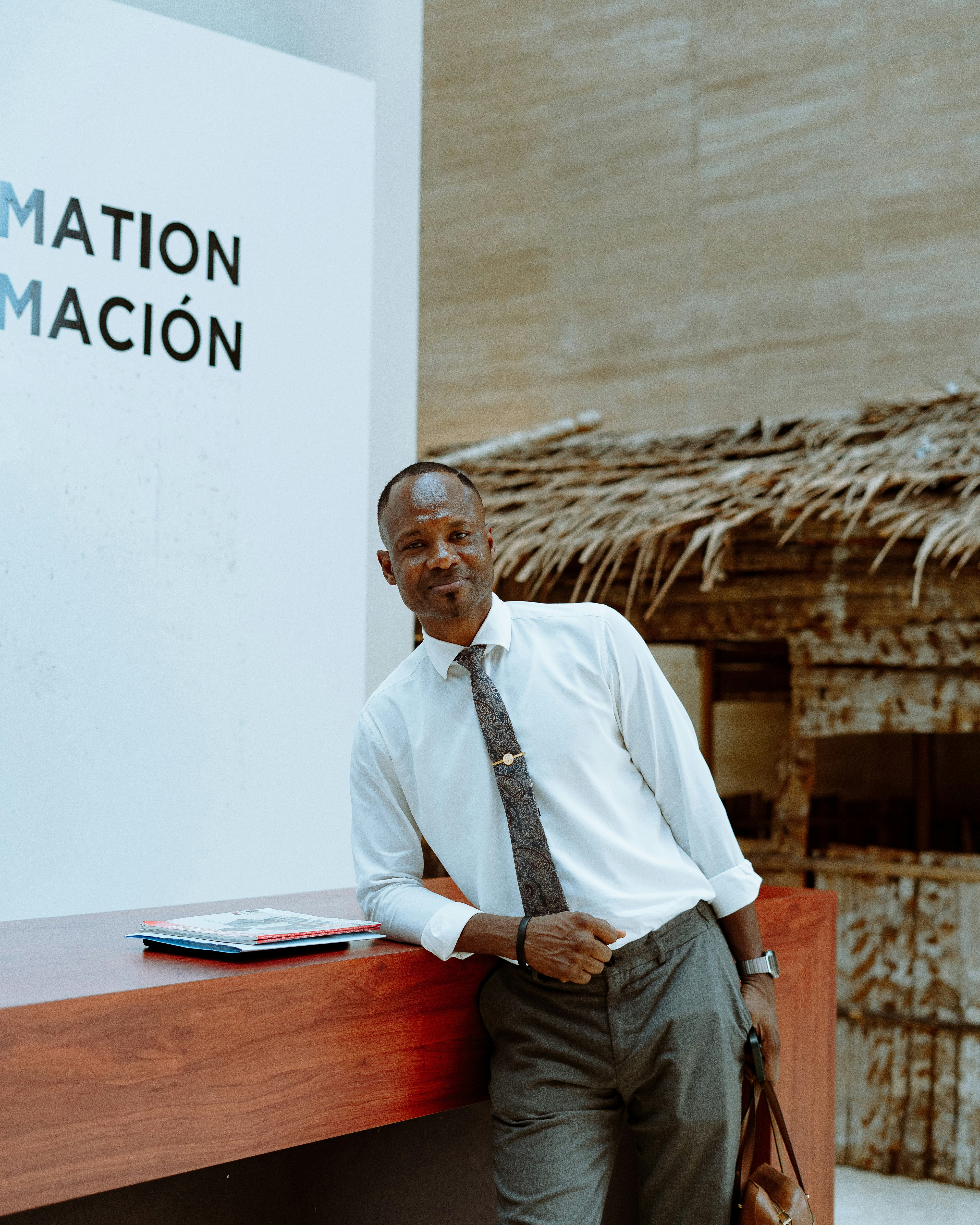 A man in a white shirt and patterned tie leaning against a wooden counter