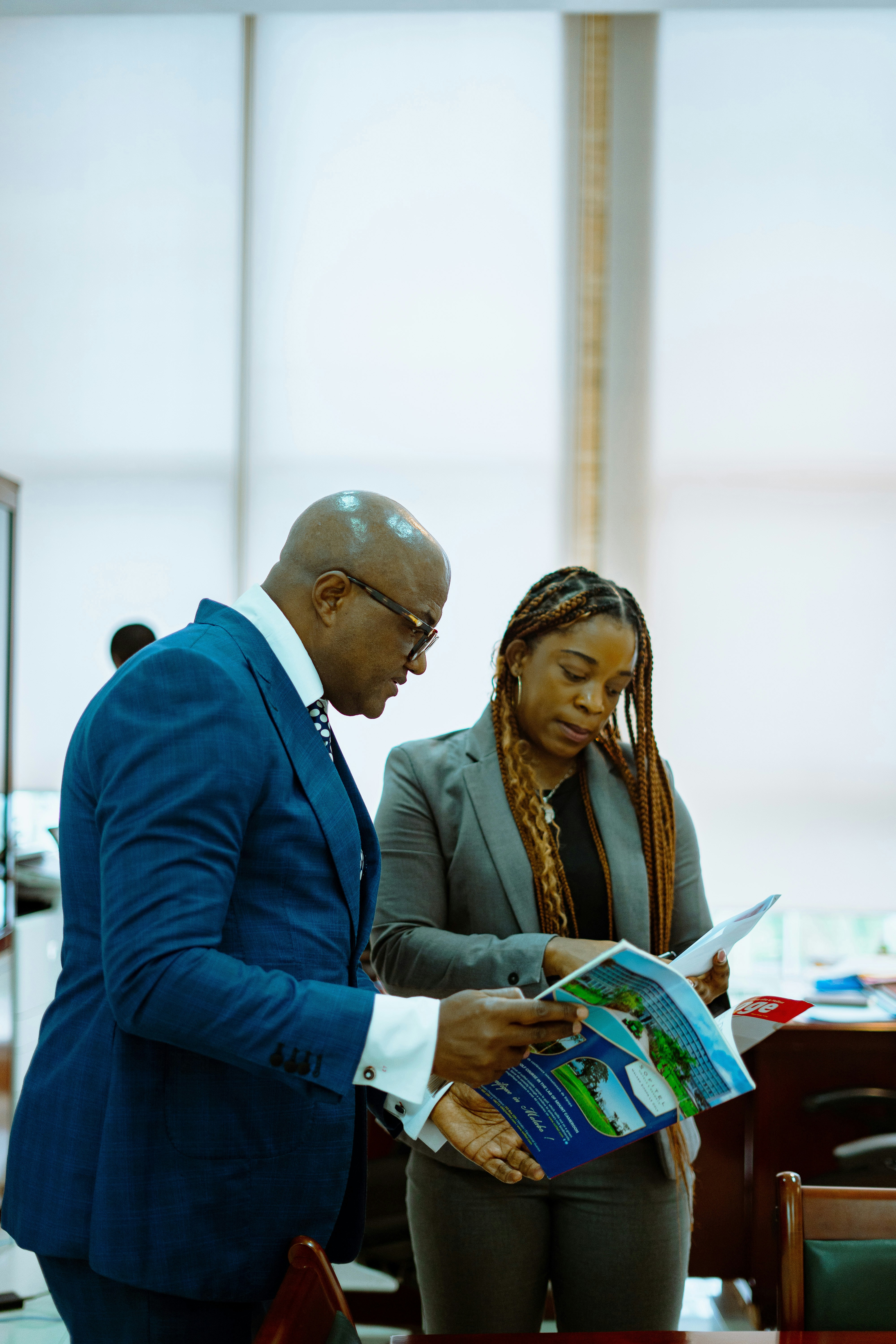 A man in a blue suit and a woman reading a brochure in an office