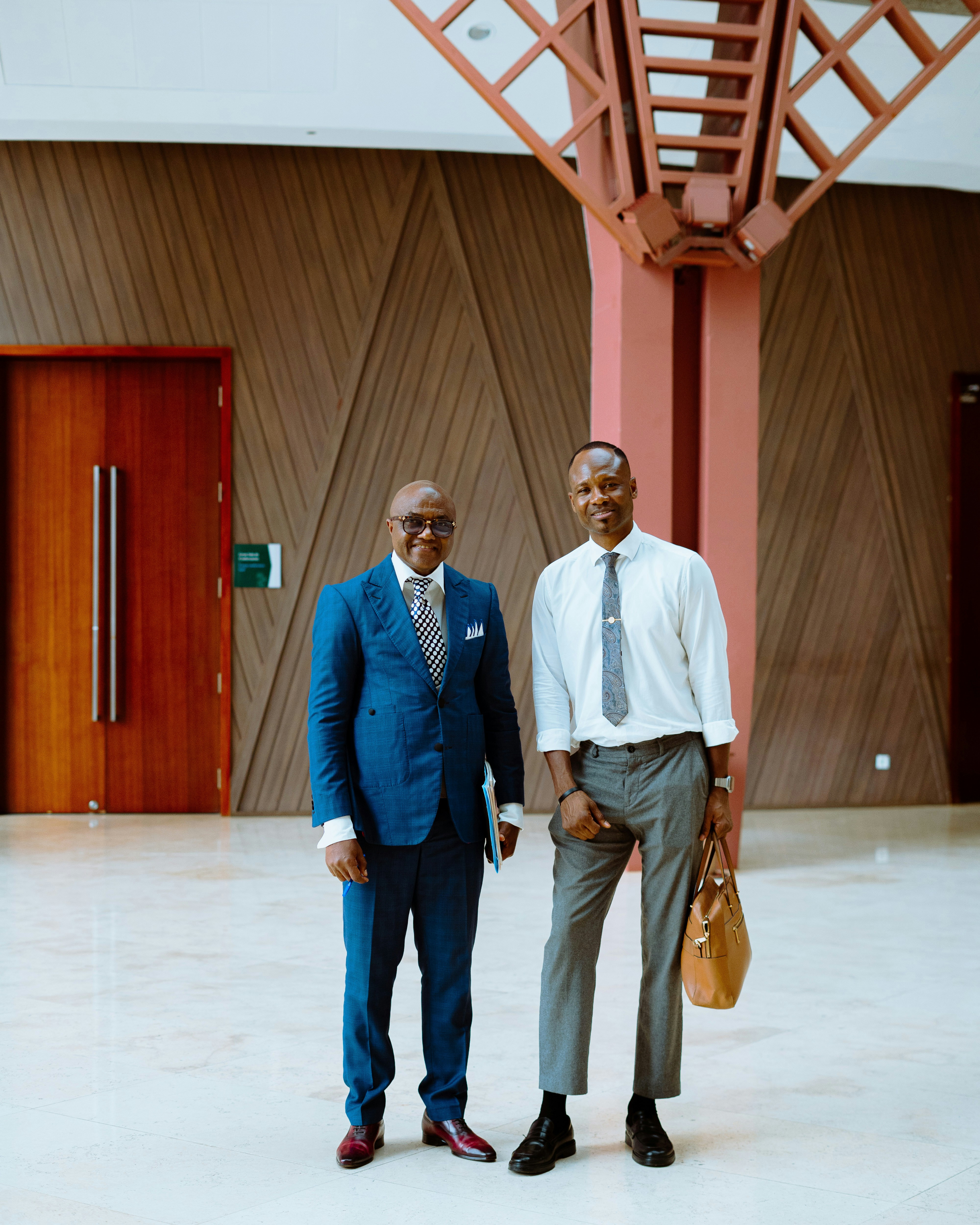 Two men in business attire standing in a modern lobby with wooden walls