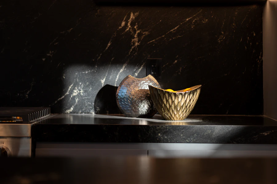 Hammered silver vase and faceted gold bowl on black marble in a slash of light