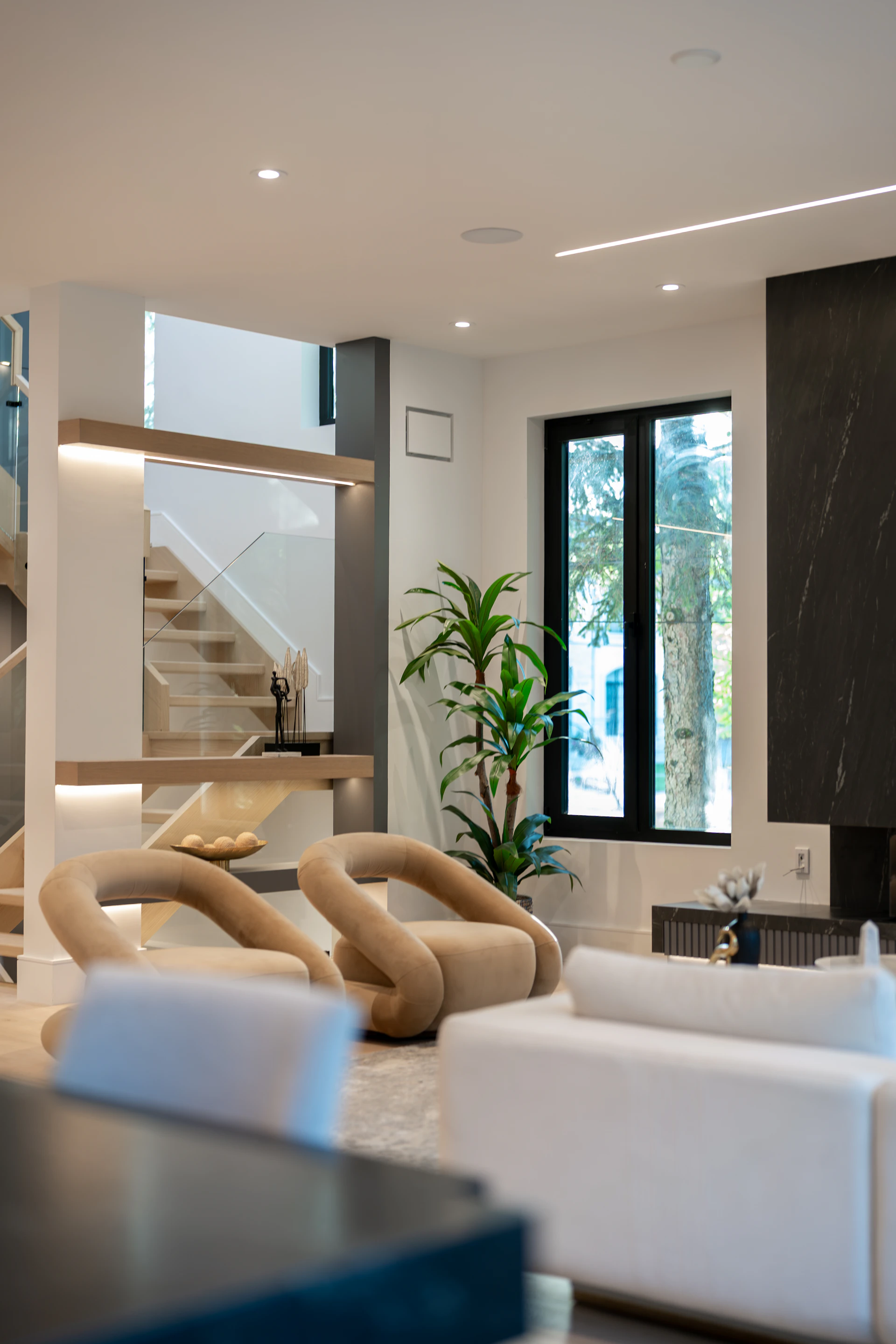 Two beige curved armchairs in a modern living room with a staircase