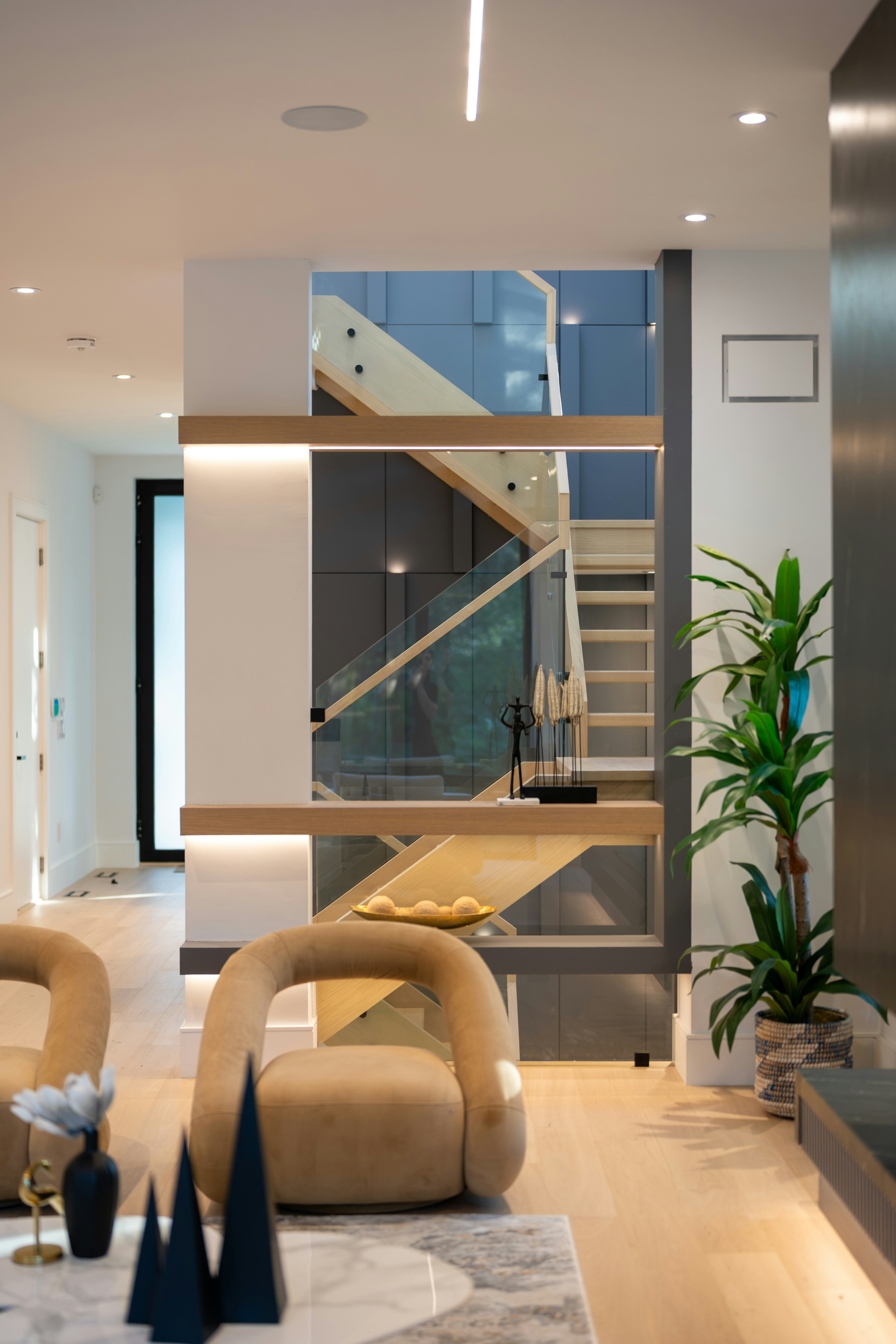 Modern living room with beige armchairs and a wooden staircase behind glass