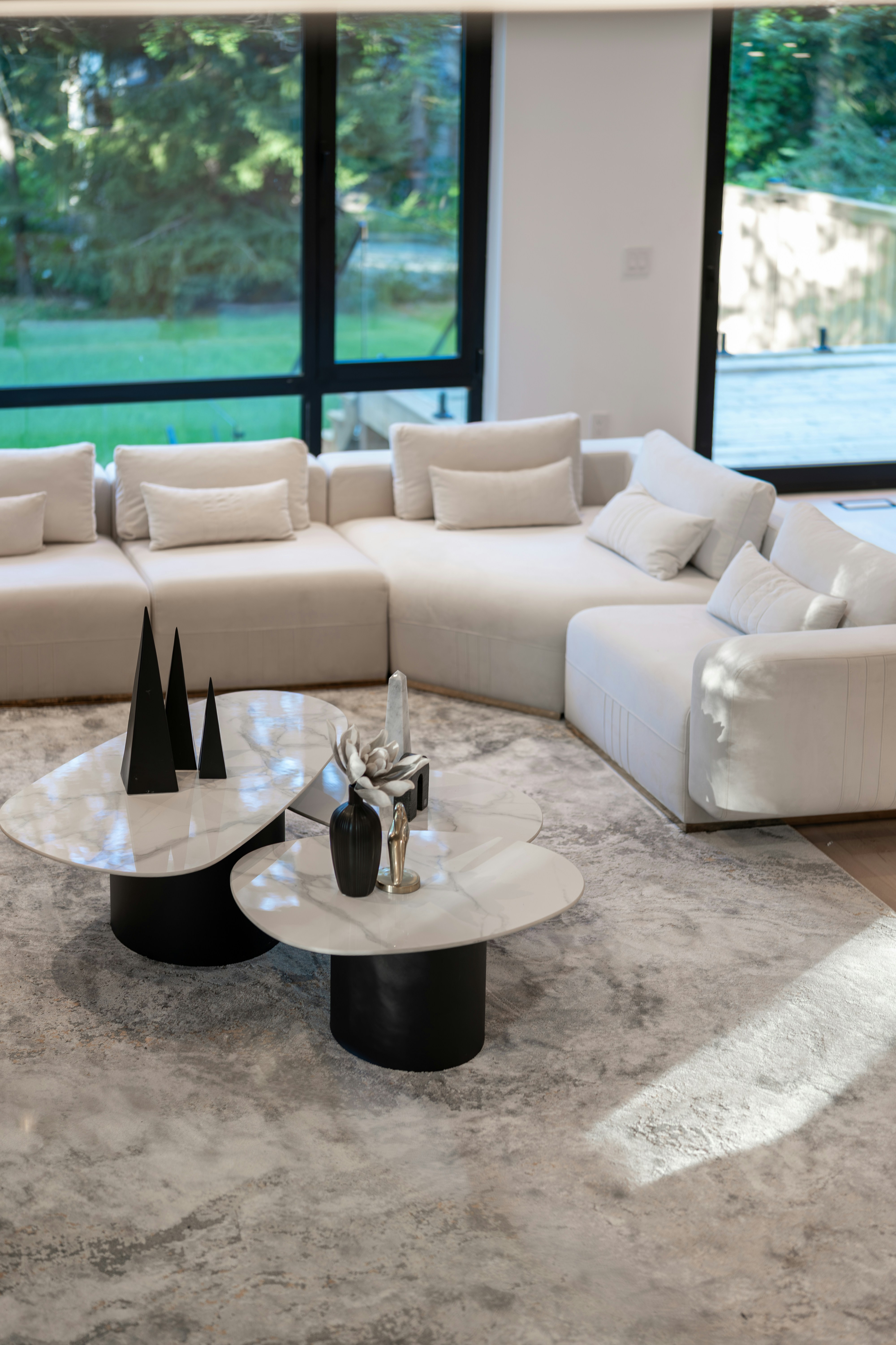 A white sectional sofa and marble coffee tables in a sunlit living room