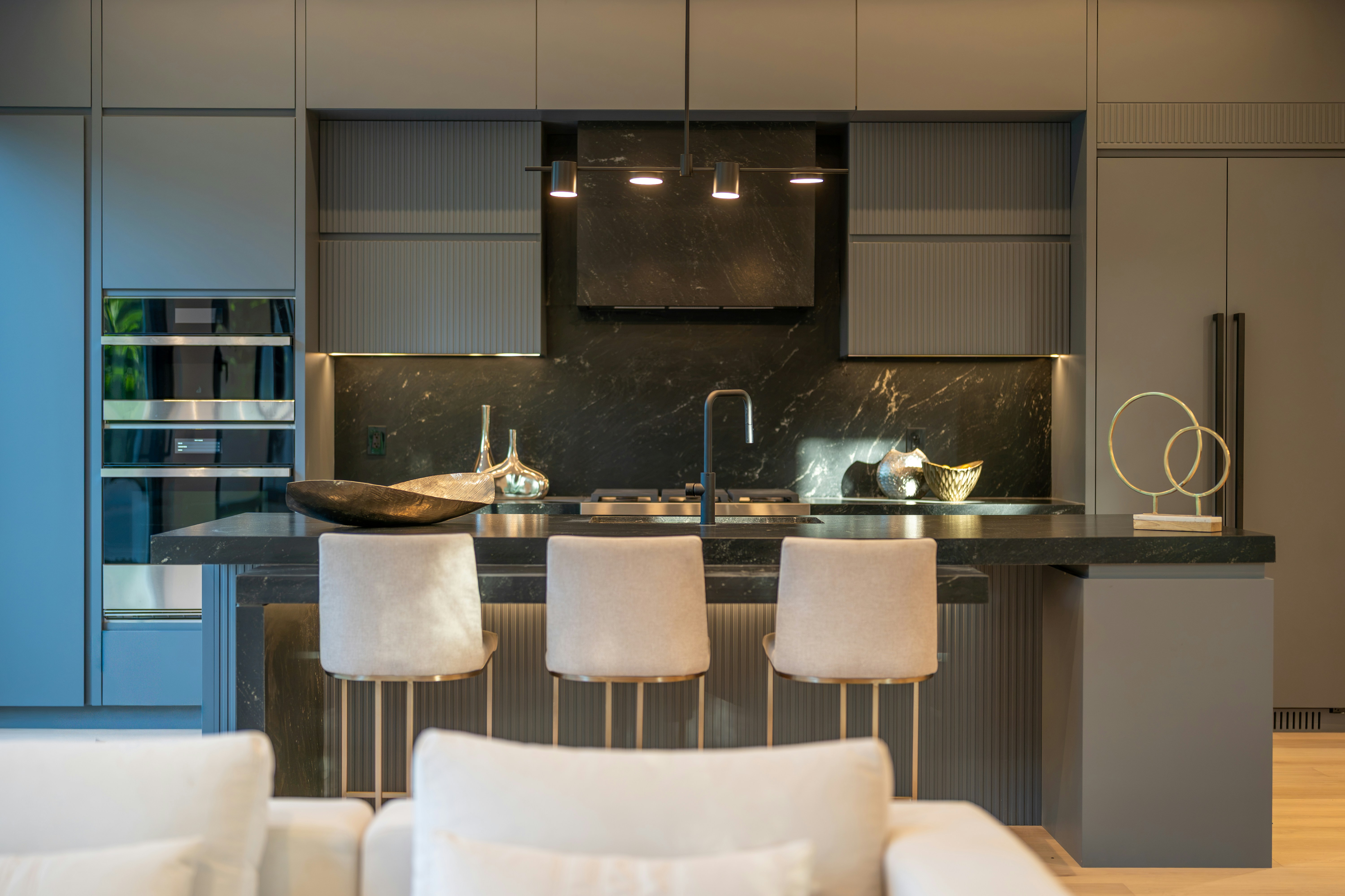 Modern kitchen with dark grey cabinetry, marble backsplash, and three upholstered bar stools