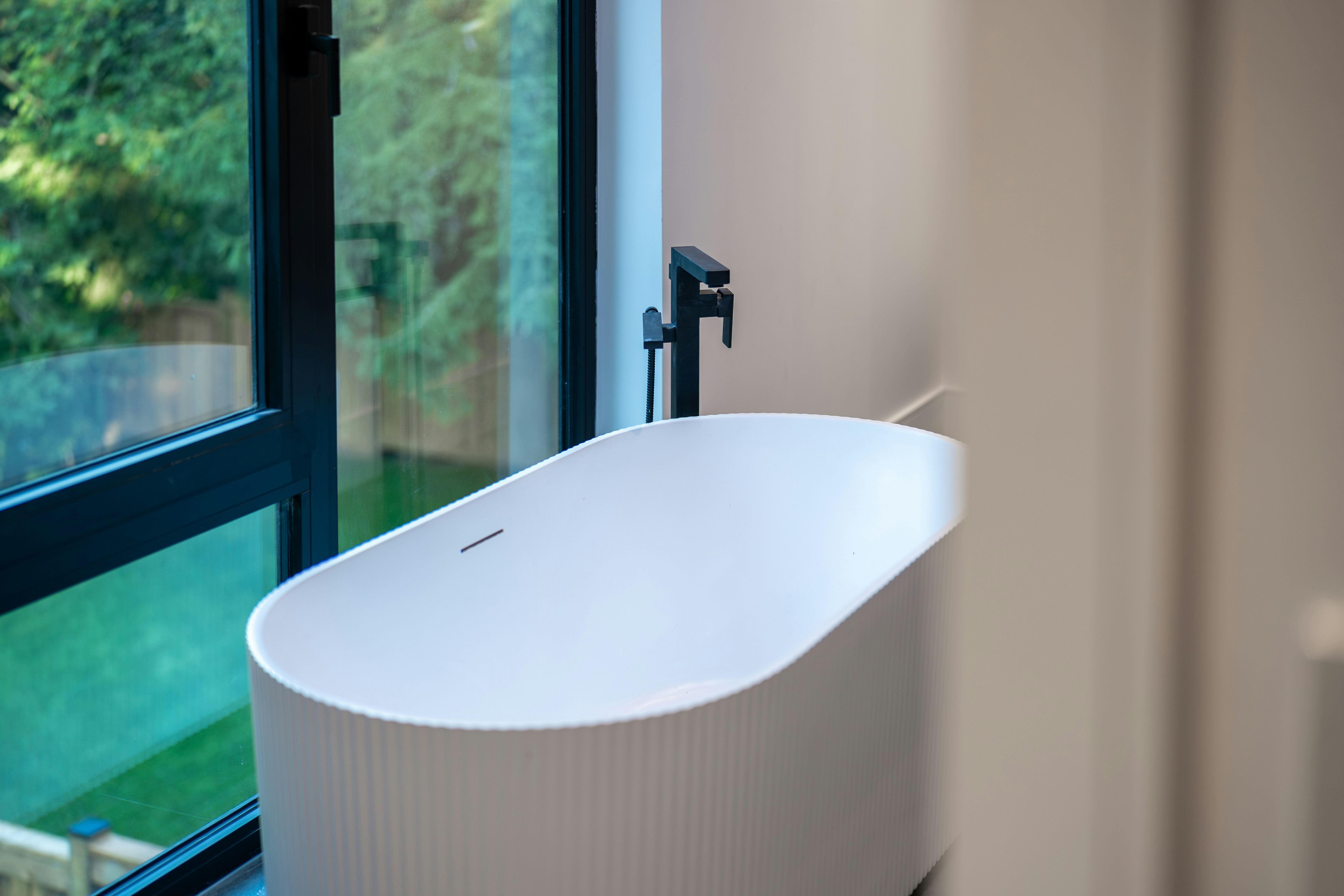 A white oval bathtub with a black faucet beside a large window