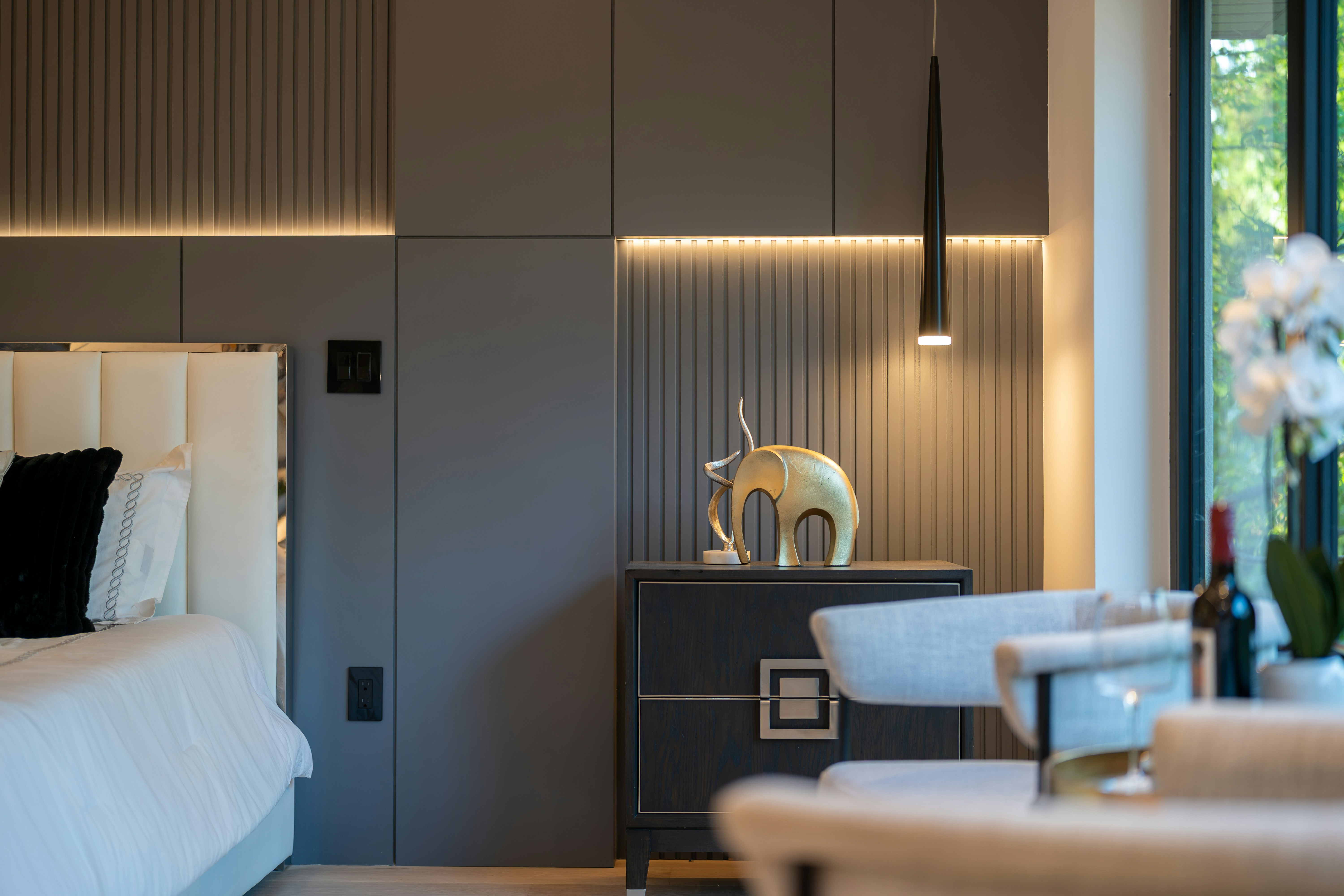 A gold elephant figurine on a dark nightstand in a modern bedroom