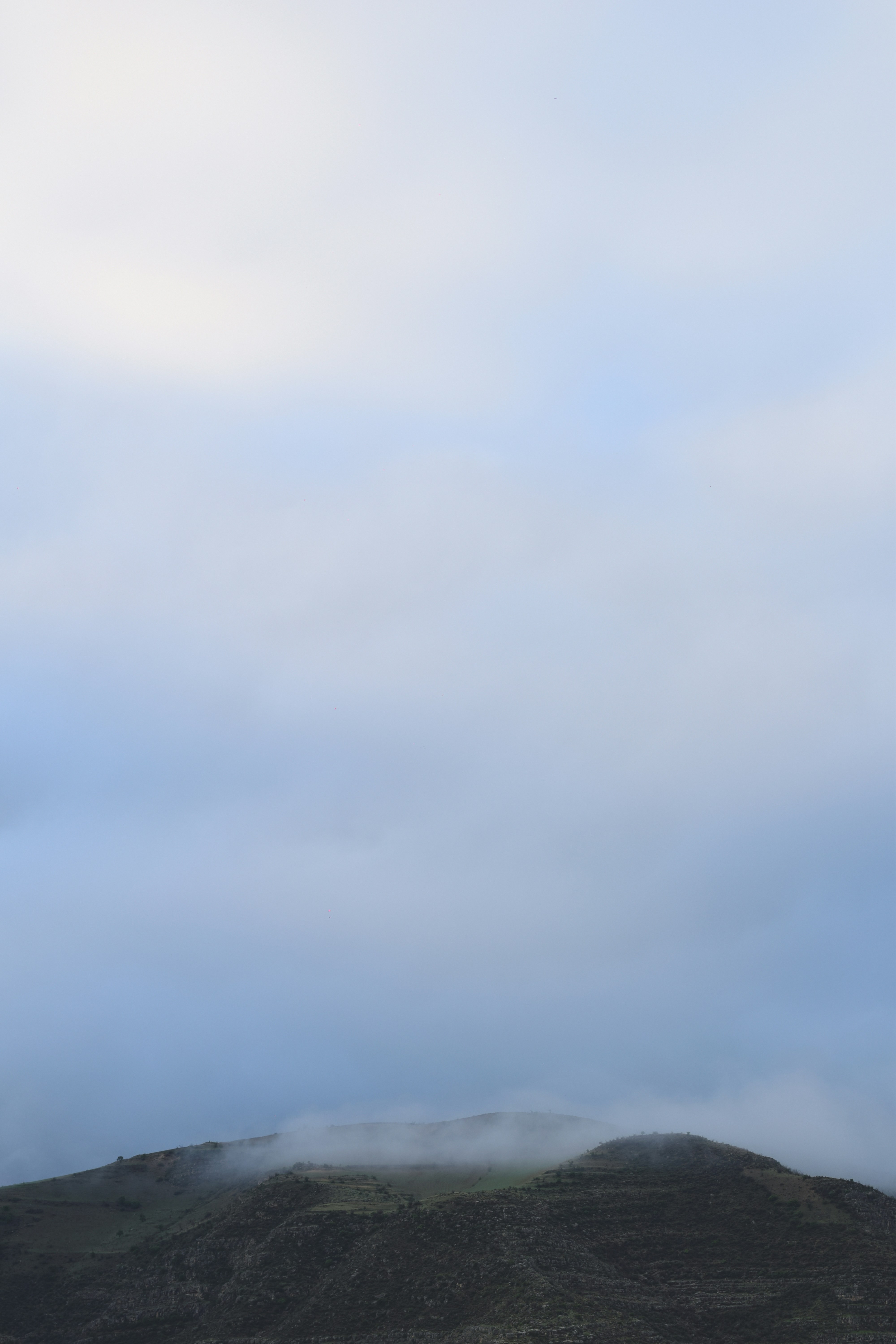 Ein niedriger Hügel mit spärlicher Vegetation unter einer dicken Schicht grauer Wolken