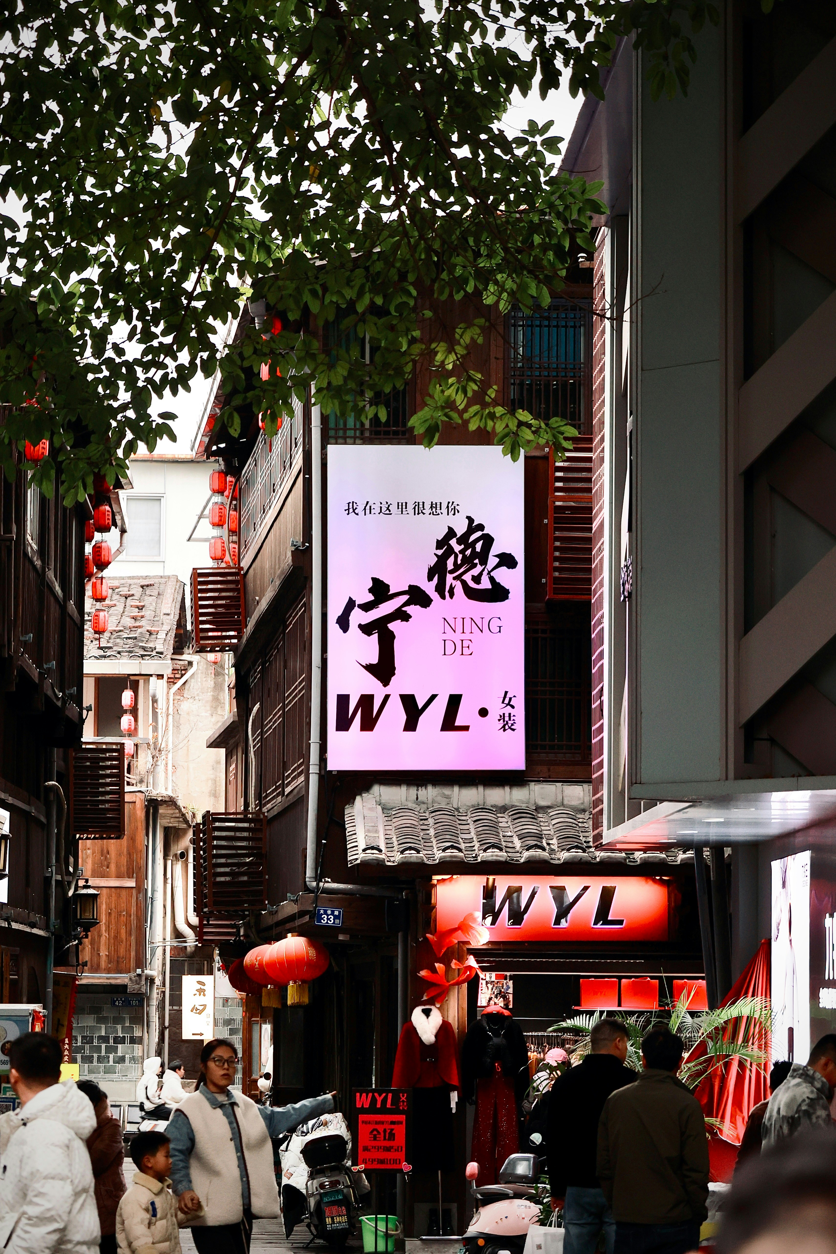People walking on a narrow street with traditional wooden buildings and glowing signs