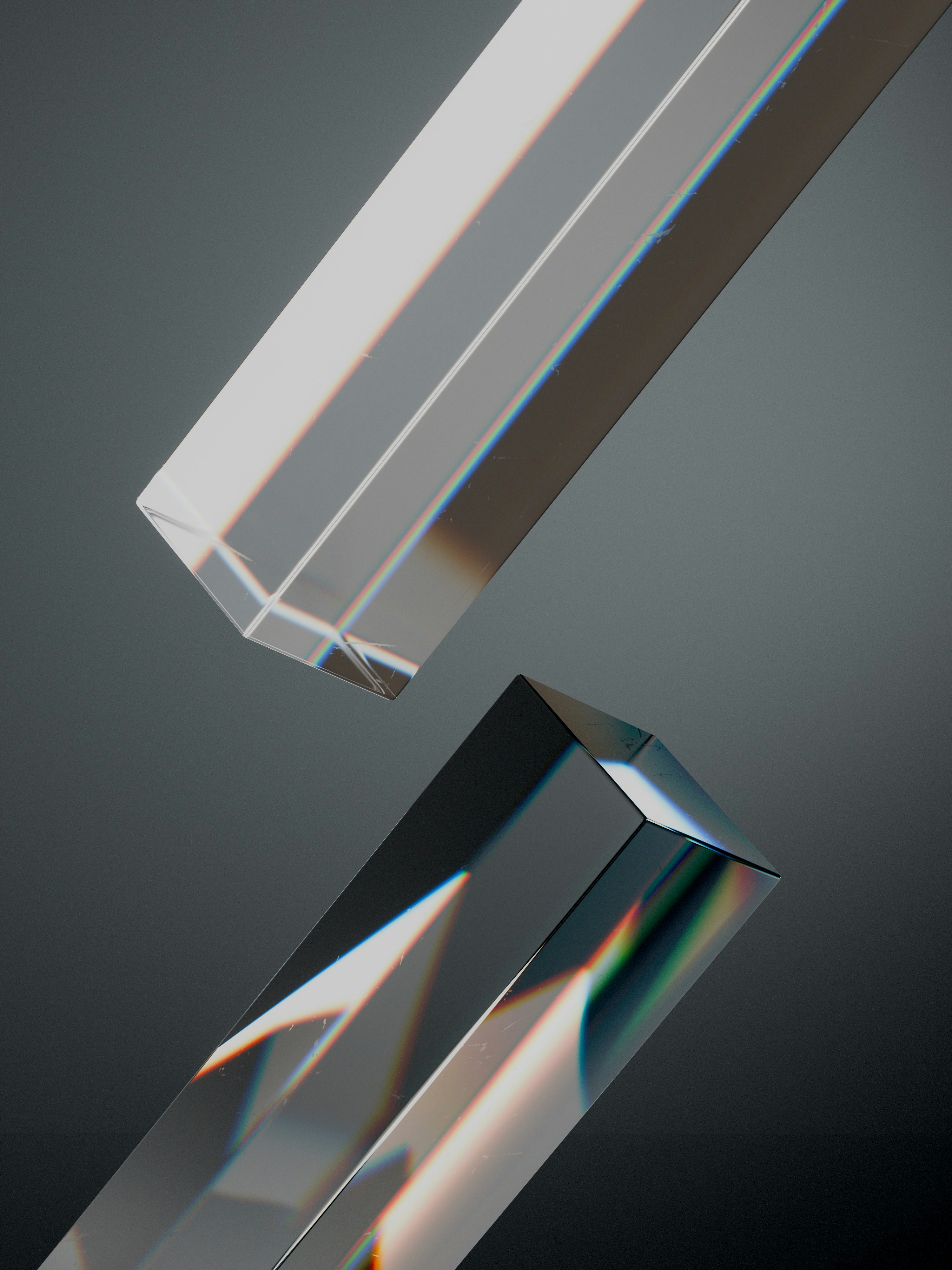 Two transparent glass prisms with rainbow light refraction against a dark grey background