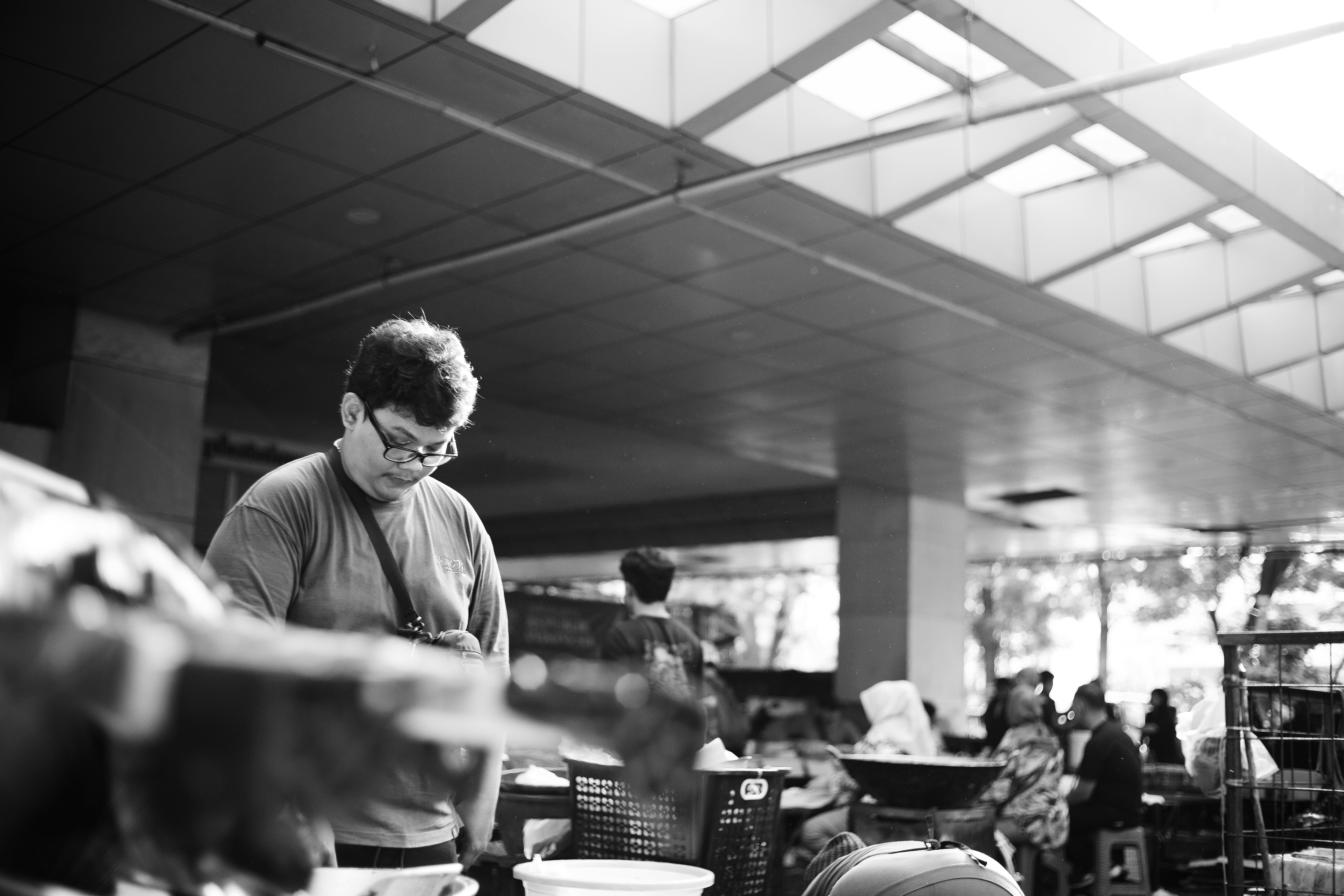 A person with glasses looking down in a busy outdoor market area