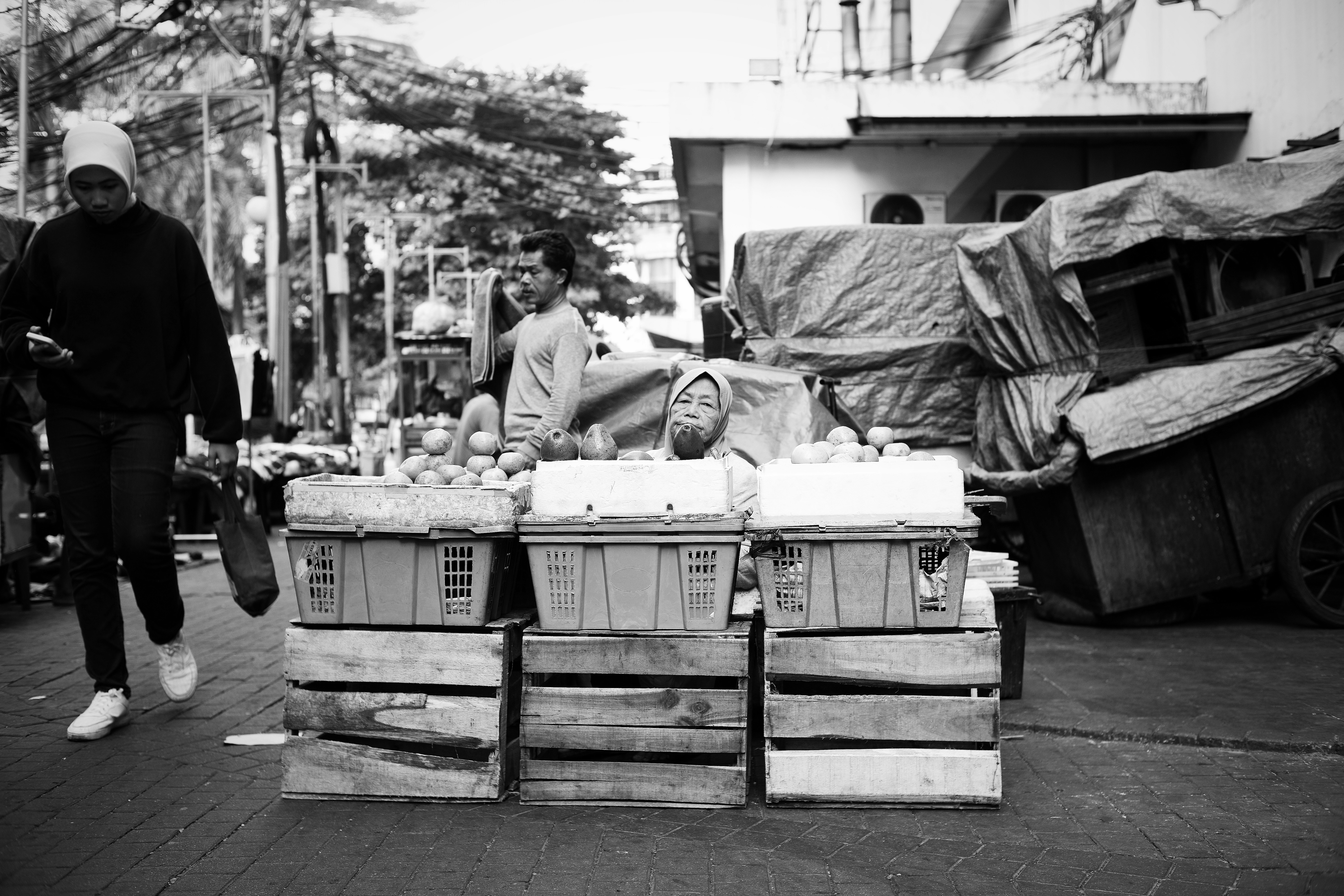 A person in a hijab selling fruit from crates on a city street