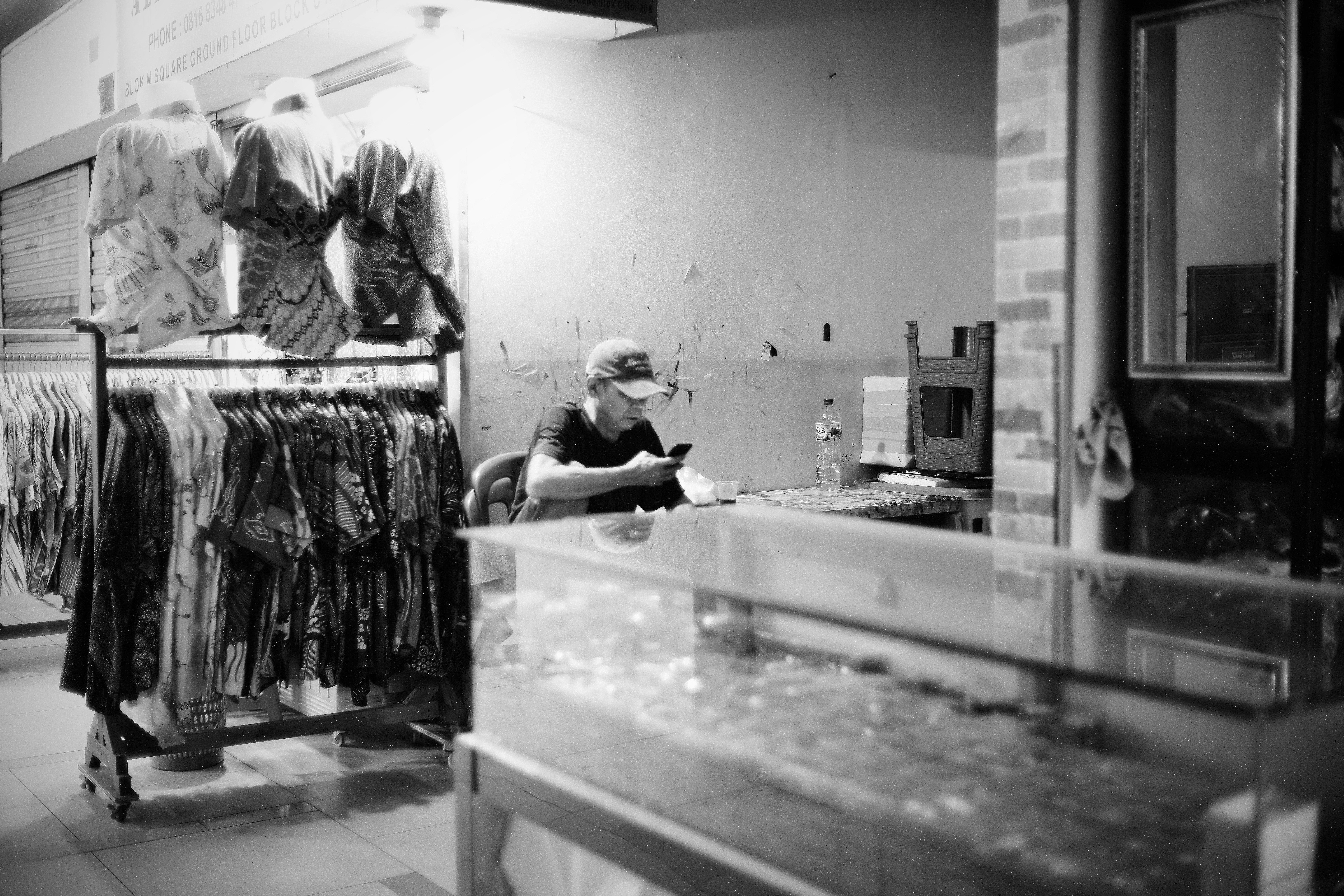 A man in a cap using a smartphone at a table in a clothing shop