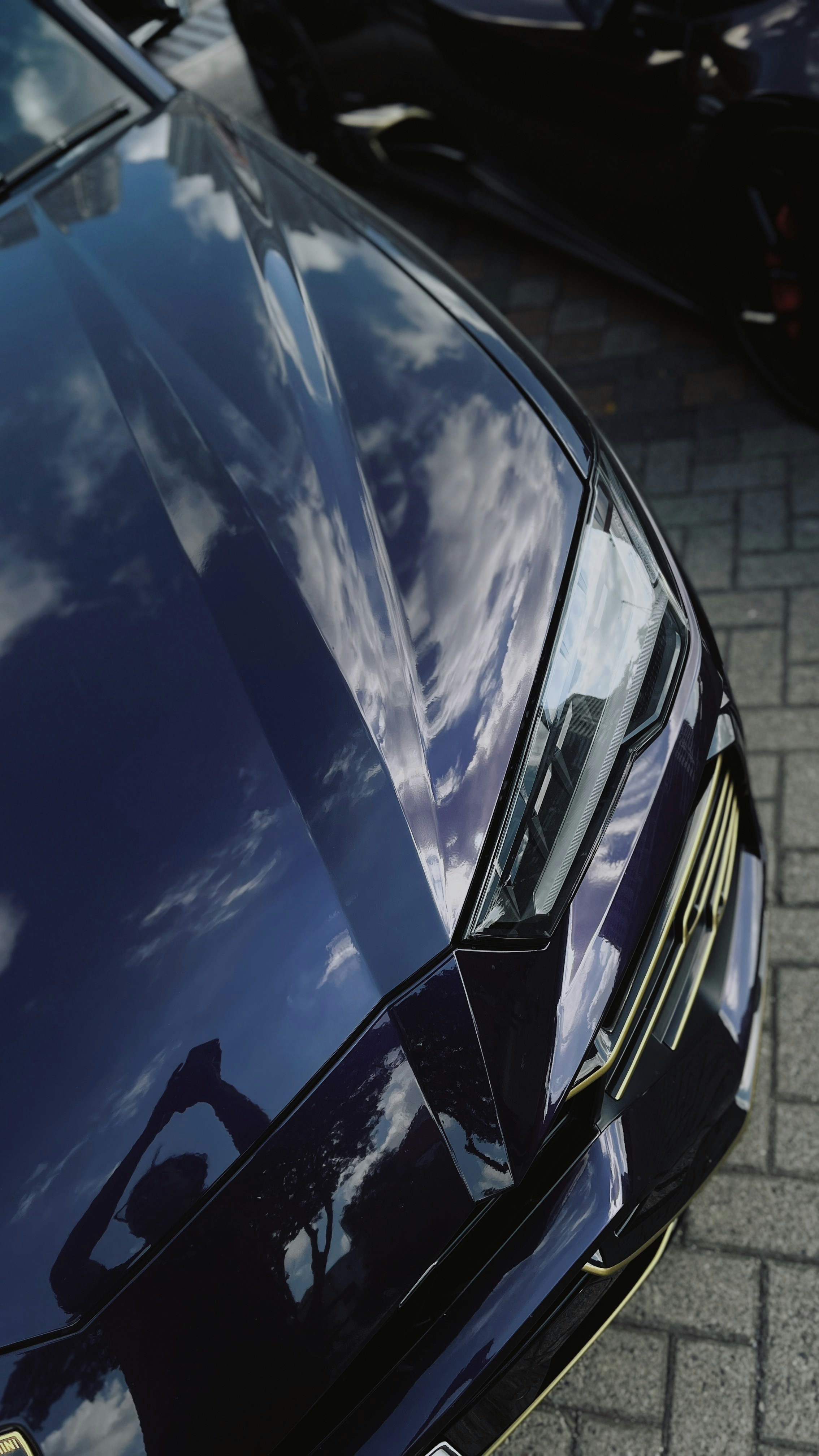 A dark purple sports car hood reflecting a blue sky with white clouds
